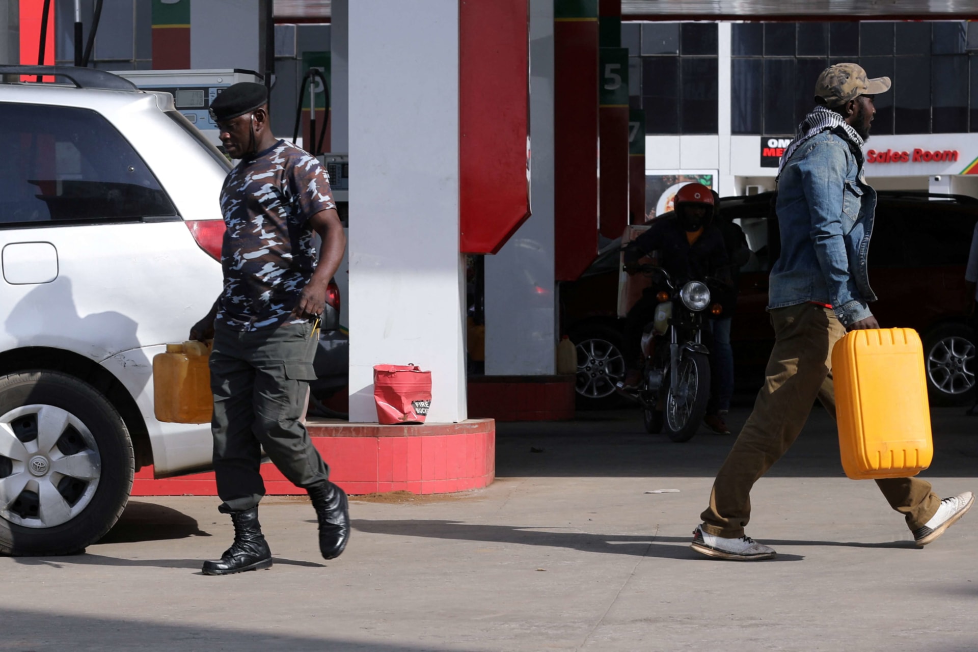 <p>A man and police officer pass one other while carrying petrol containers at a station in Abuja, Nigeria on February 15, 2022.</p>
