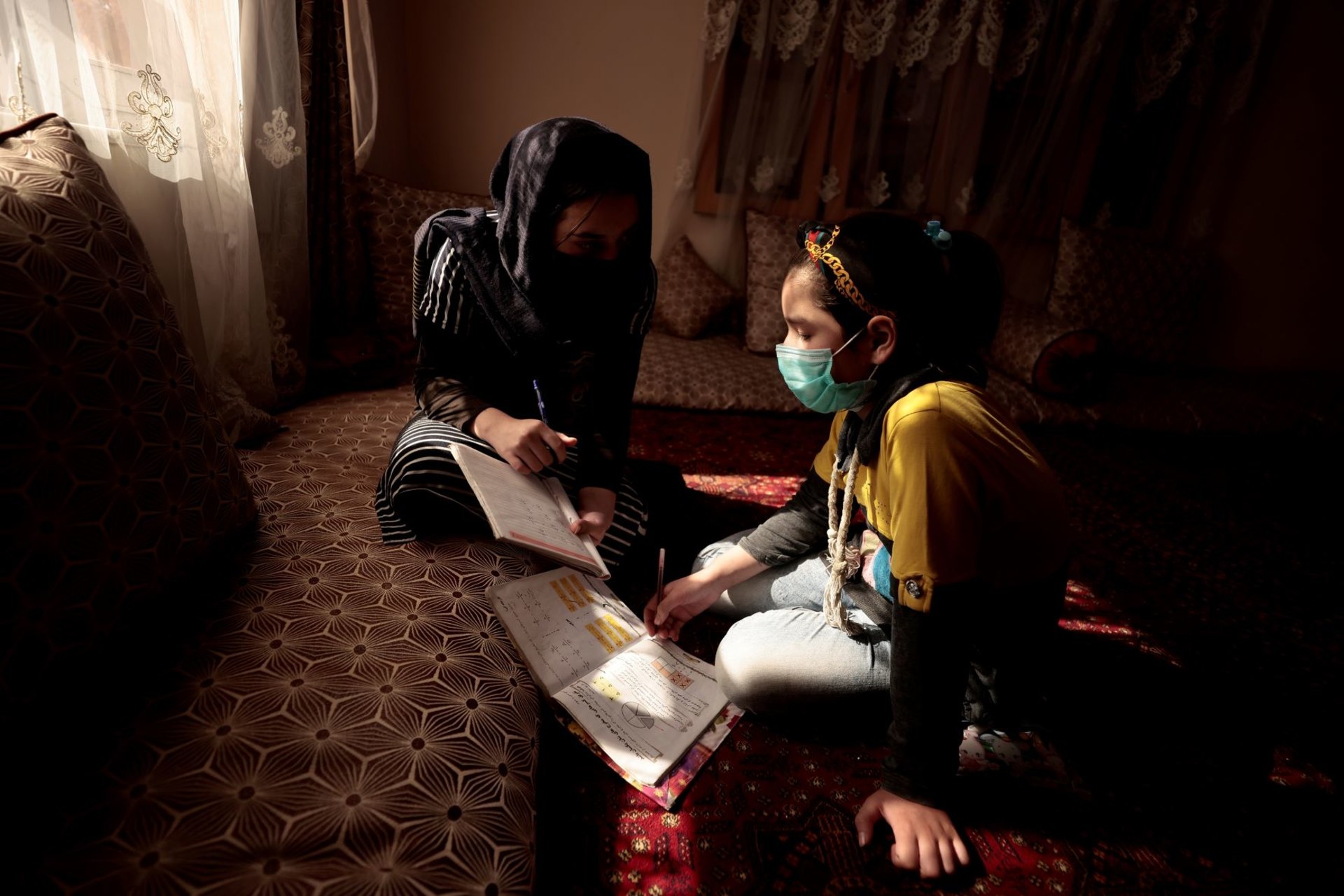 <p>Sahar, 17, helps her sister, Hadia, 10, with her homework after school at their home in Kabul, Afghanistan on October 26, 2021.</p>
