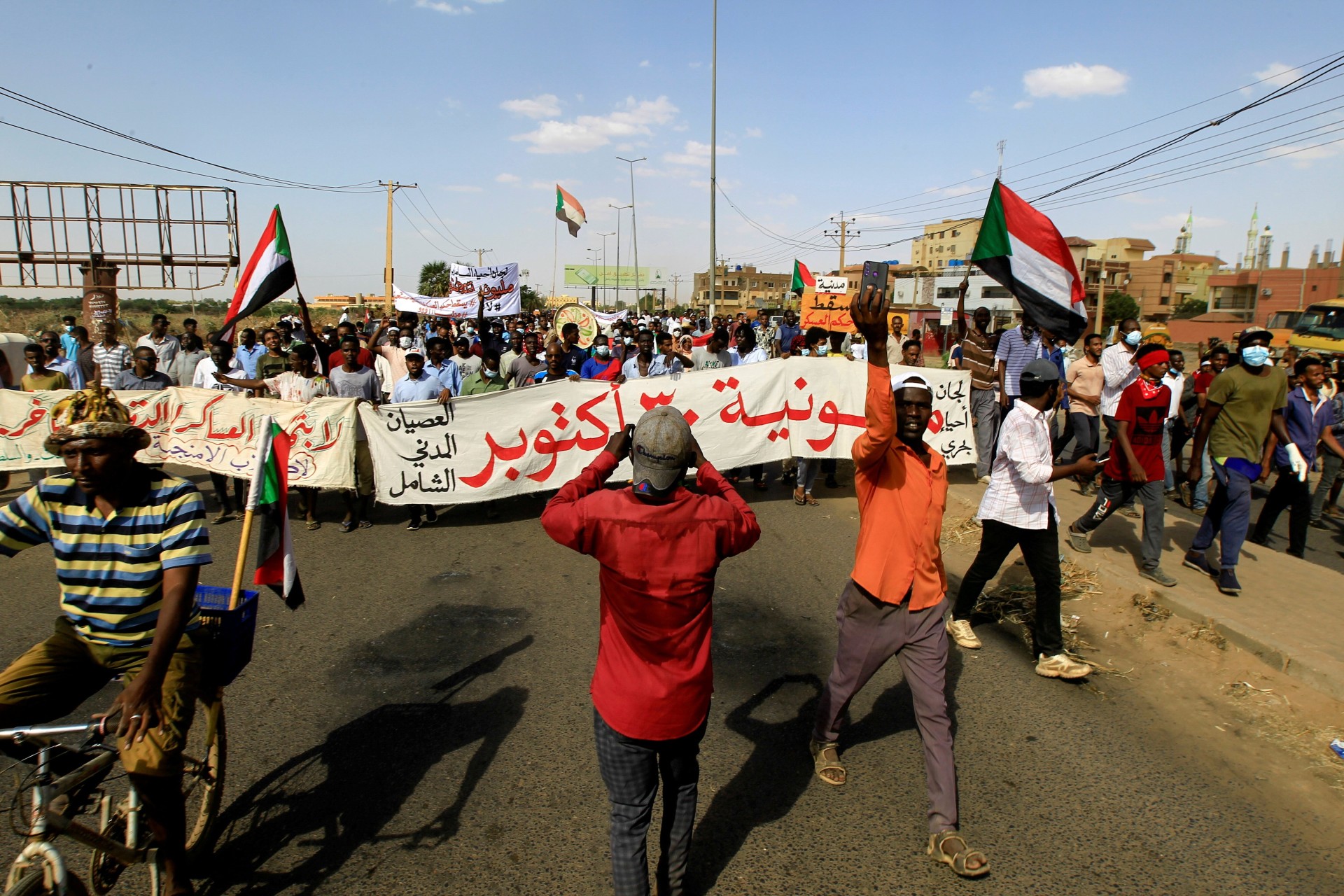 <p>Protesters carry a banner and national flags as they march against the Sudanese military’s recent seizure of power and ousting of the civilian government, in the streets of the capital Khartoum, Sudan on October 30, 2021.</p>