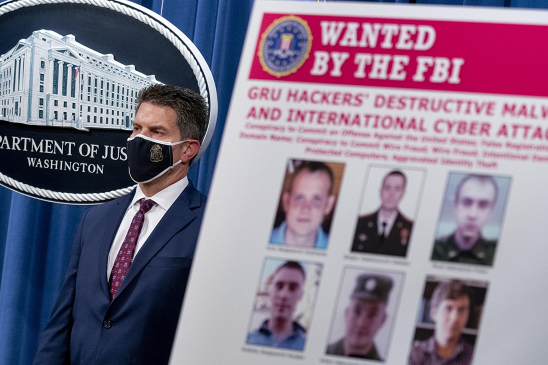 <p>A poster showing six wanted Russian military intelligence officers is displayed with FBI Deputy Director David Bowdich in the background</p>
