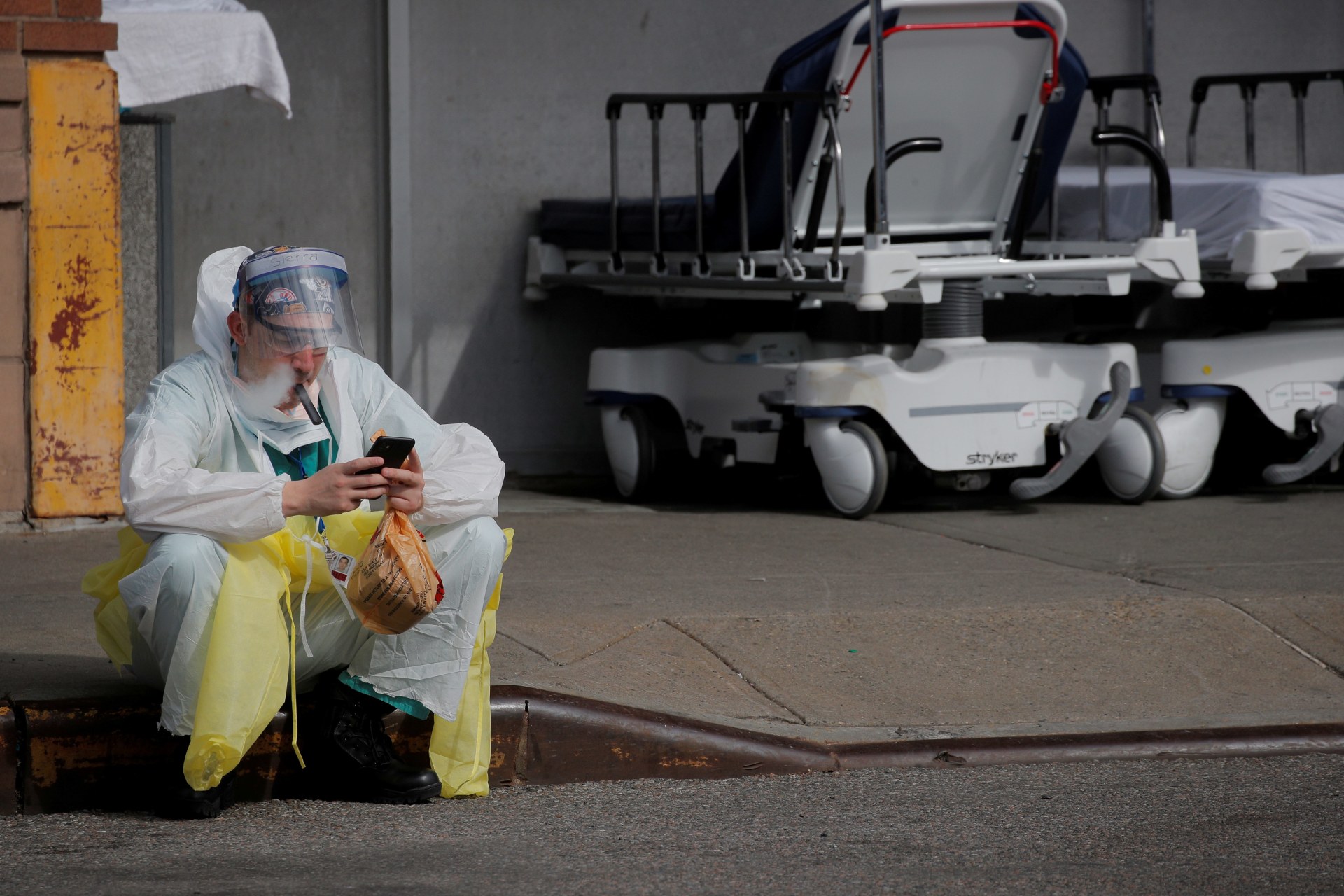 <p>A healthcare worker sits on the curb as he uses a vaping device while taking a break outside Maimonides Medical Center.</p>