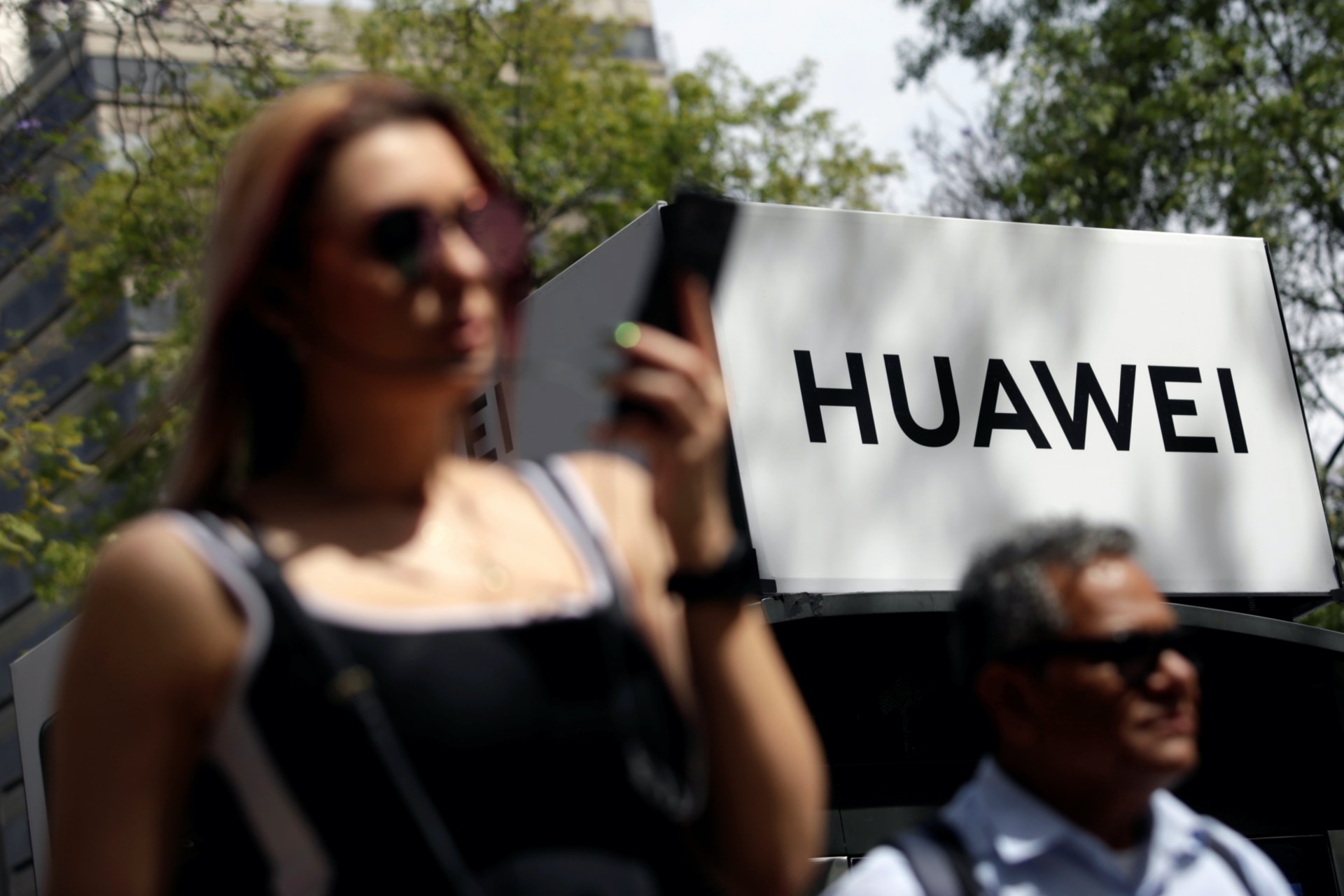 <p>People walk past a Huawei company logo at a bus stop in Mexico City on February 22, 2019.</p>