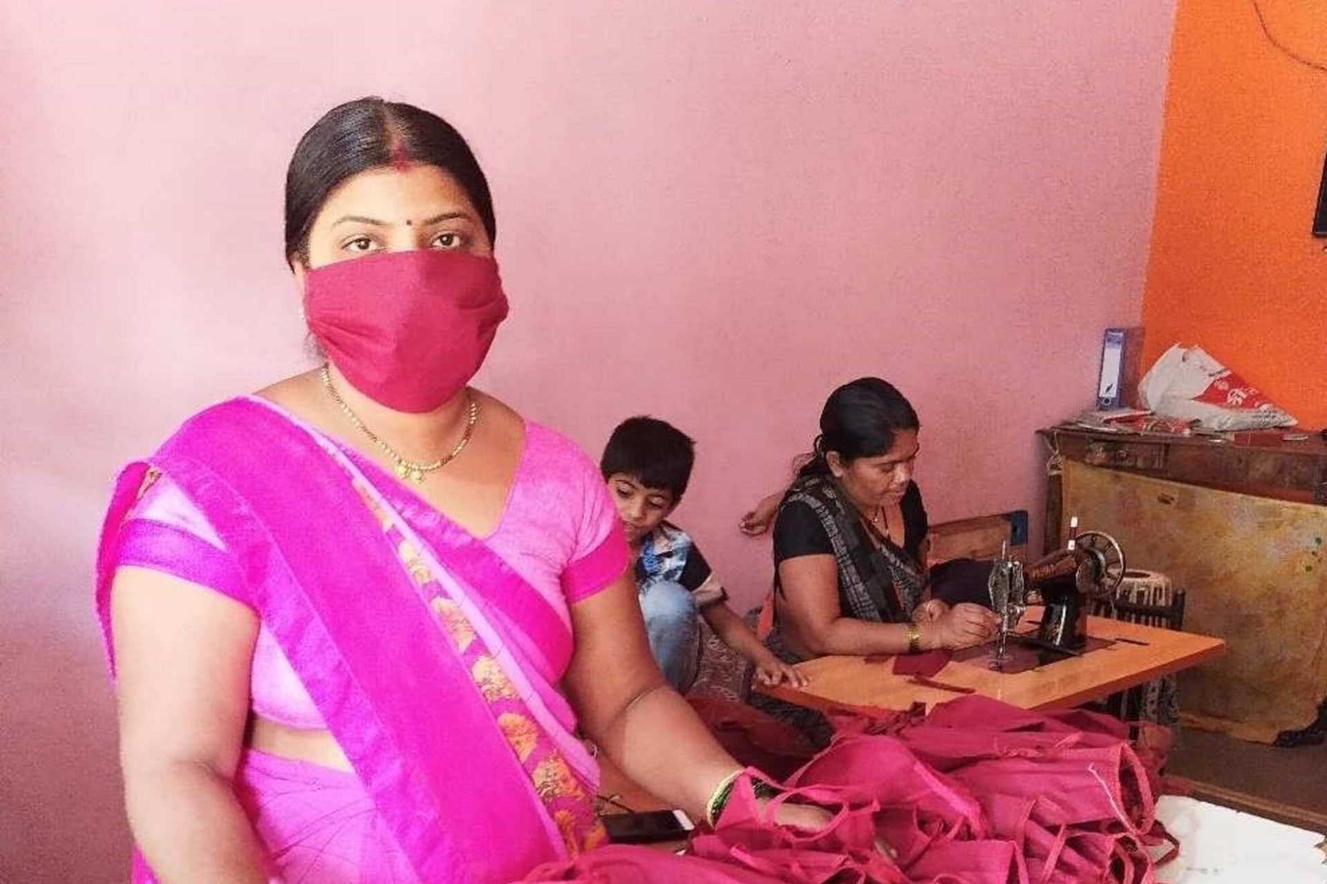 <p>Woman stands behind face masks sewn by members of the Self-Employed Women’s Association (SEWA) in India.</p>
