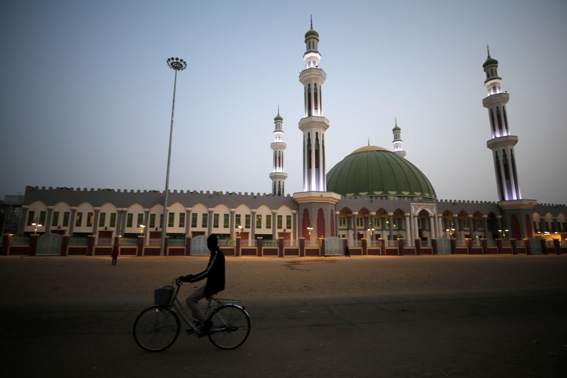 <p>A man cycles past the Al Ansar mosque in Maiduguri, Nigeria, on February 16, 2019. Both Yusuf and Adam preached there in the early 2000s.</p>