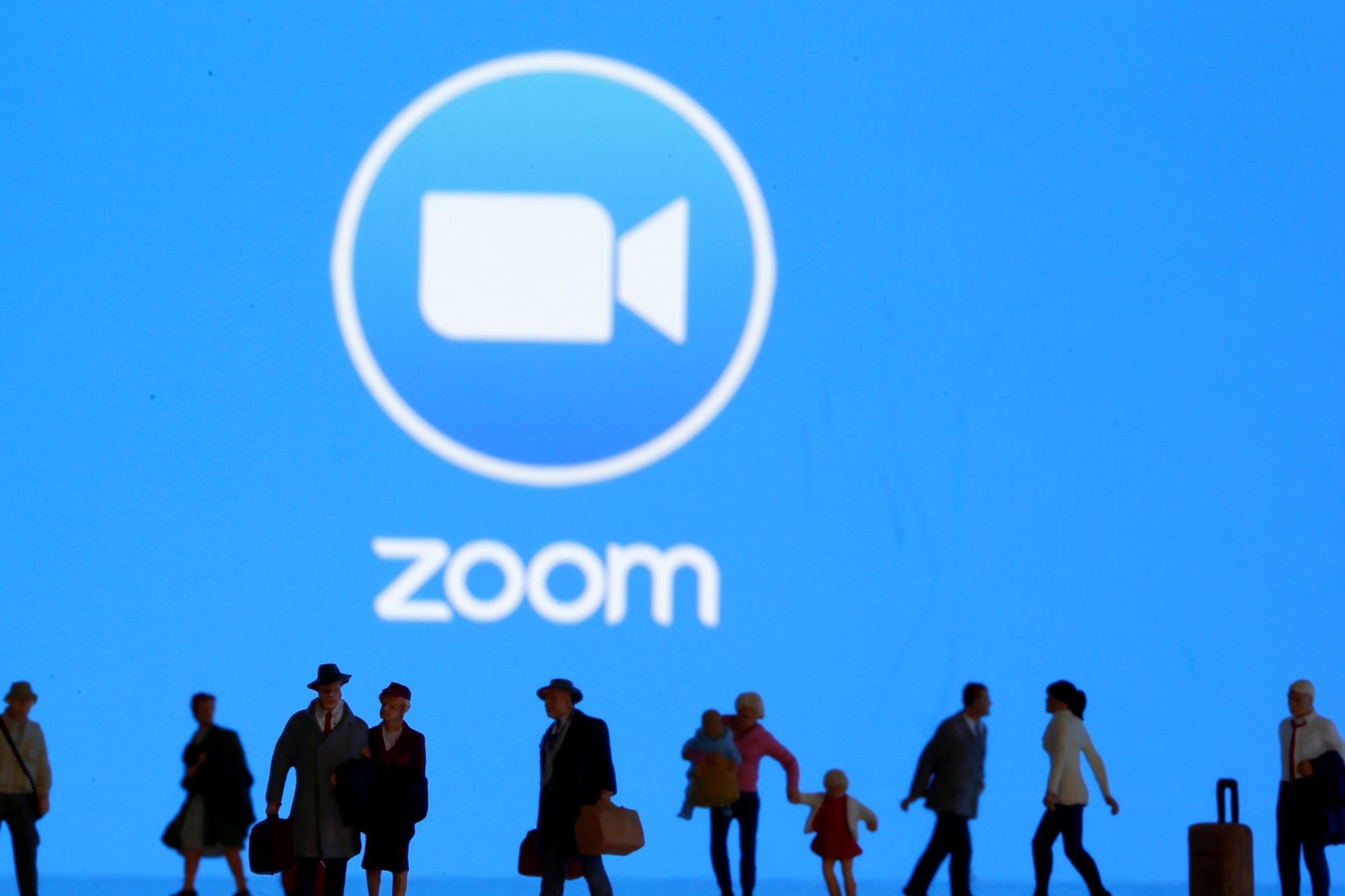 <p>Small toy figures are seen in front of diplayed Zoom logo.</p>

