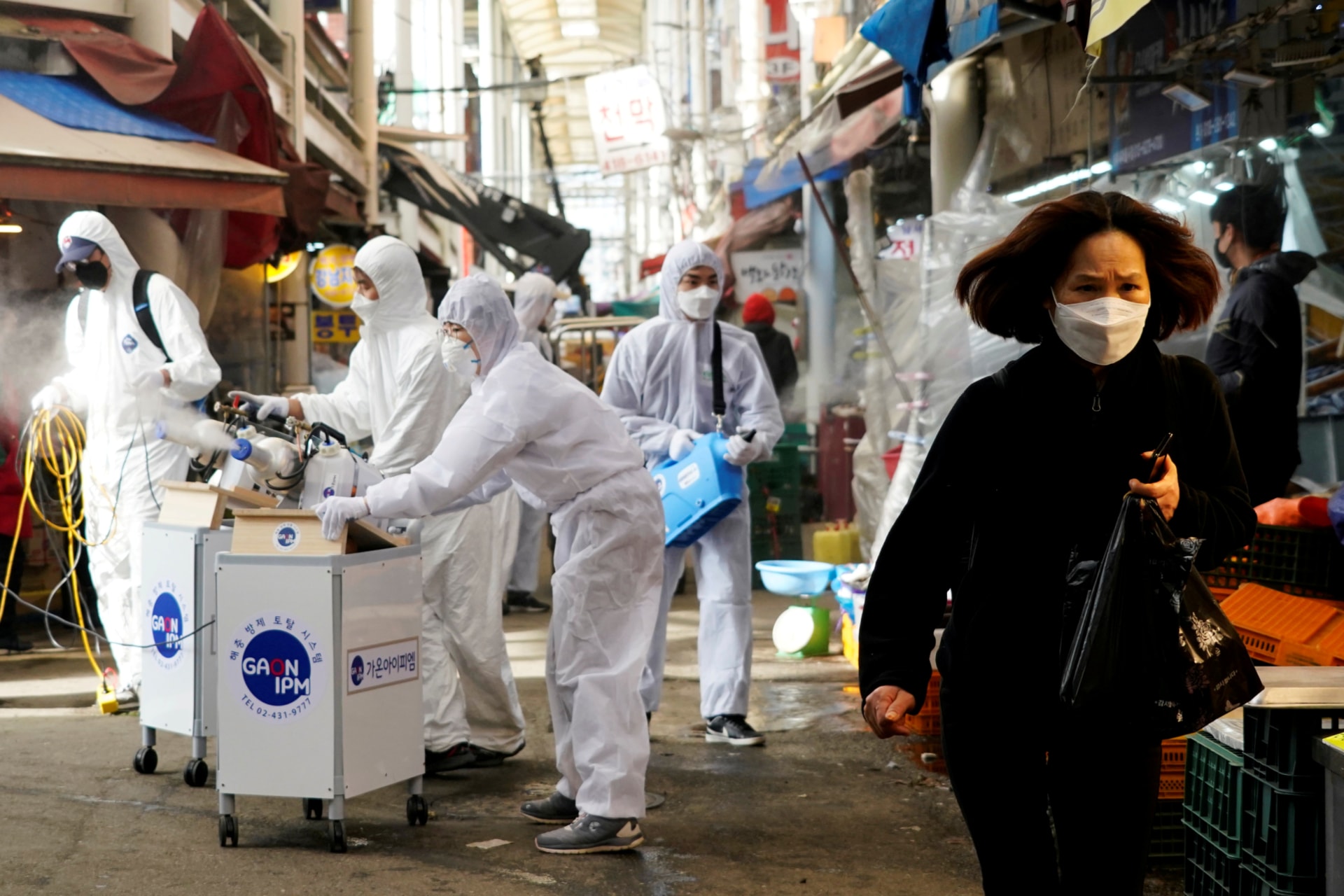 <p>A woman wearing a mask to prevent contracting the coronavirus reacts as employees from a disinfection service company sanitize a traditional market in Seoul, South Korea, on February 26, 2020.</p>
