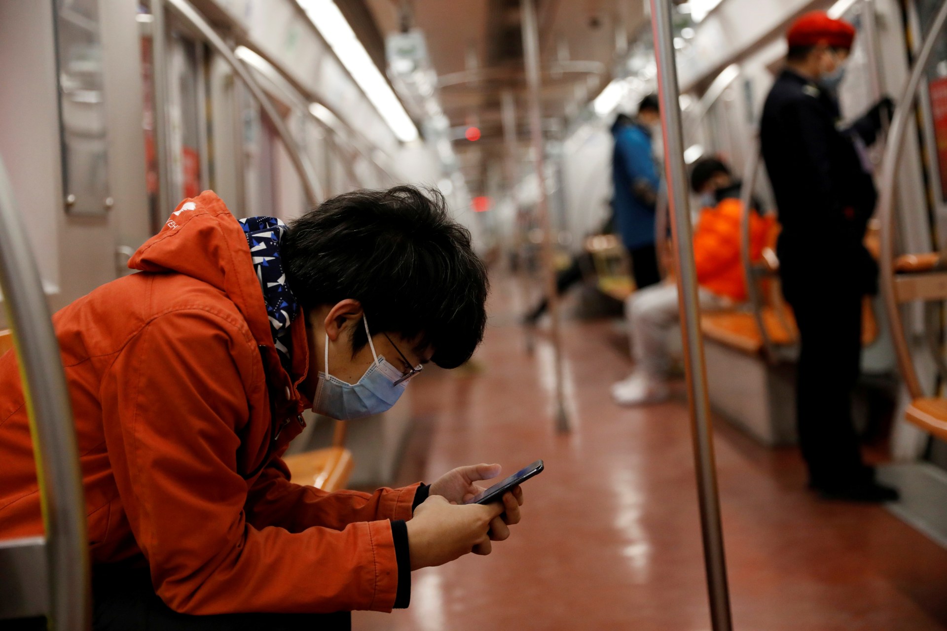 <p> A man wearing a face mask checks his mobile phone while riding a subway in the morning</p>
