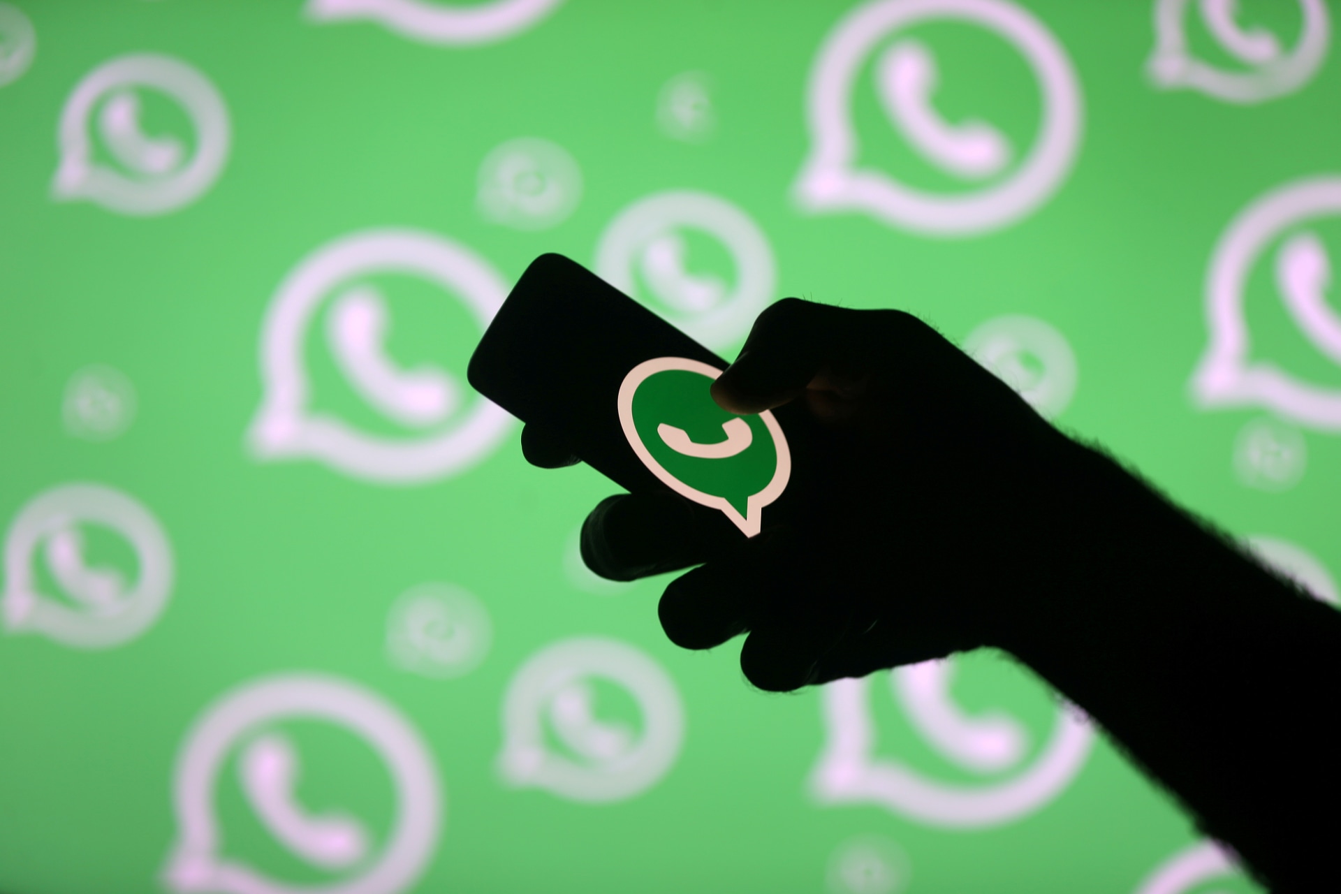 <p>A man poses with a smartphone in front of displayed Whatsapp logo in this illustration</p>