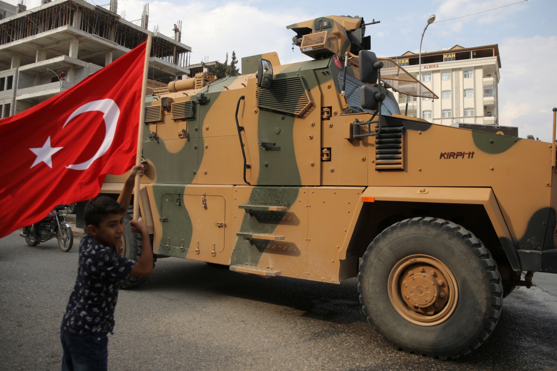 <p>A boy waves a Turkish flag as a Turkish military vehicle drives through a town near the Turkey-Syria border on October 16. </p>

