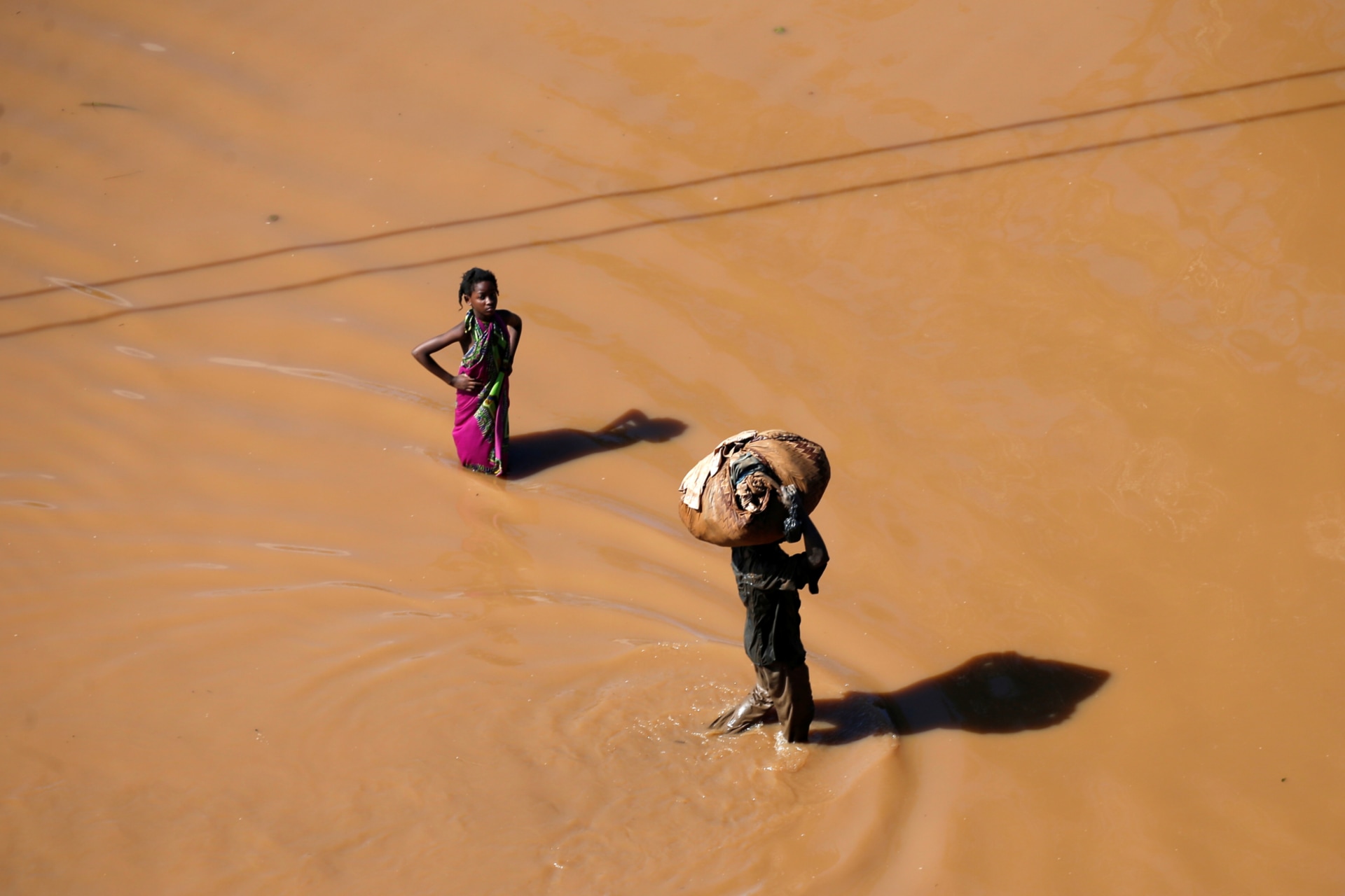 <p>A girl stops to look as a man walks past carrying luggage on his head after Cyclone Idai in Buzi district outside Beira, Mozambique, on March 22, 2019.</p>