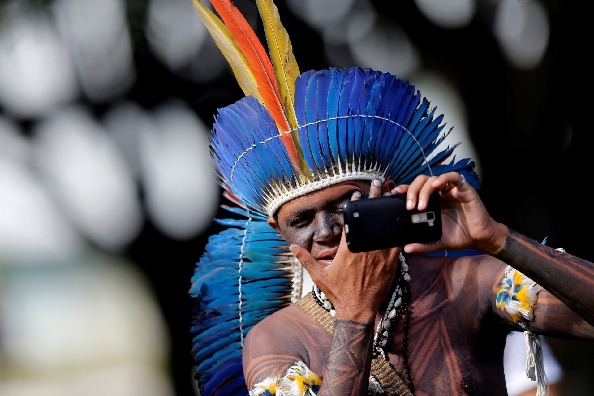 <p>A Brazilian Indigenou checks his face in a mobile phone at the Terra Livre camp, or Free Land camp in Brasilia, Brazil on April 23, 2018</p>