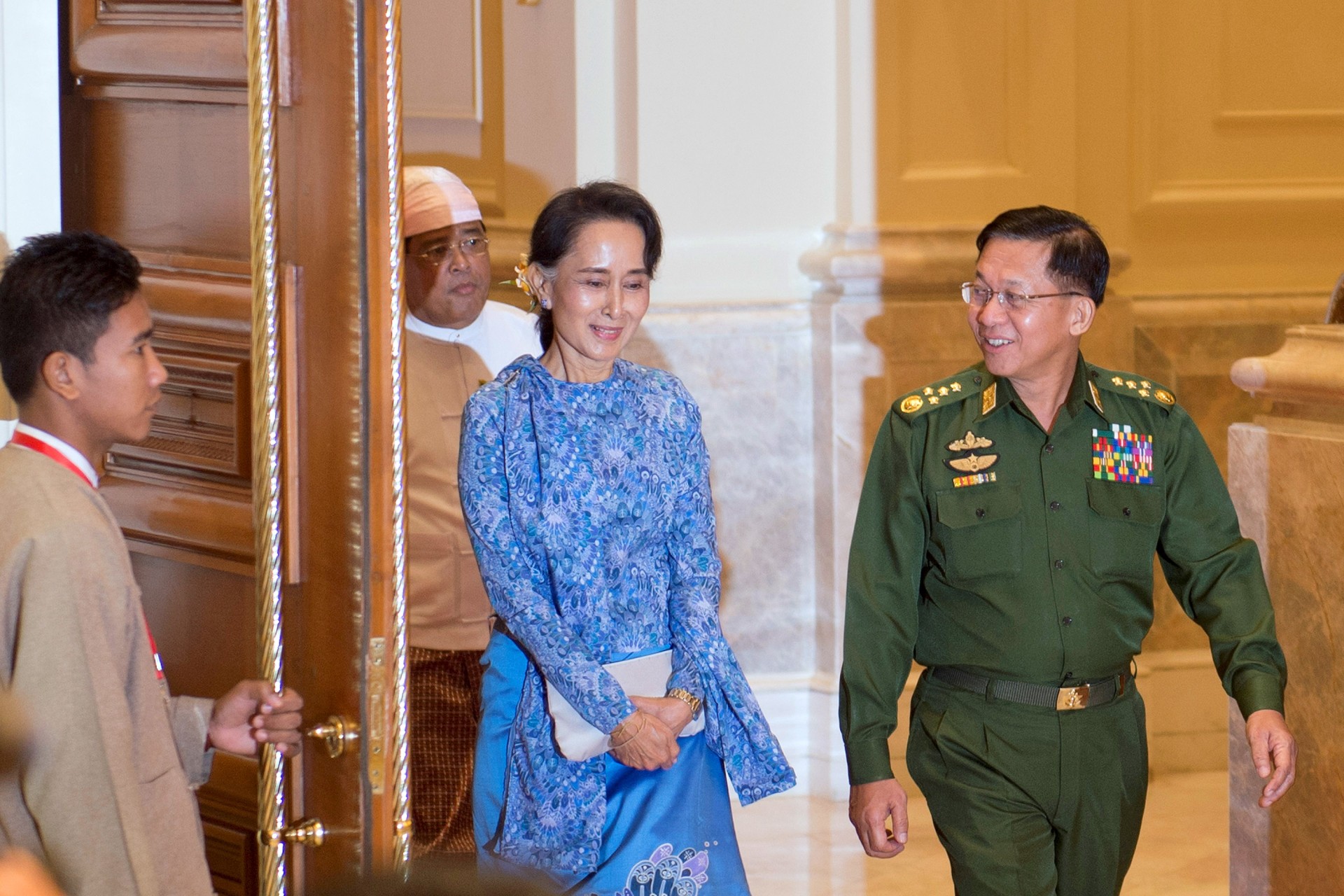<p>Aung San Suu Kyi (C) and Myanmar Military Chief Senior General Min Aung Hlaing arrive (R) for the handover ceremony from outgoing President Thein Sein and new Myanmar President Htin Kyaw at the presidential palace in Naypyitaw on March 30, 2016.</p>
