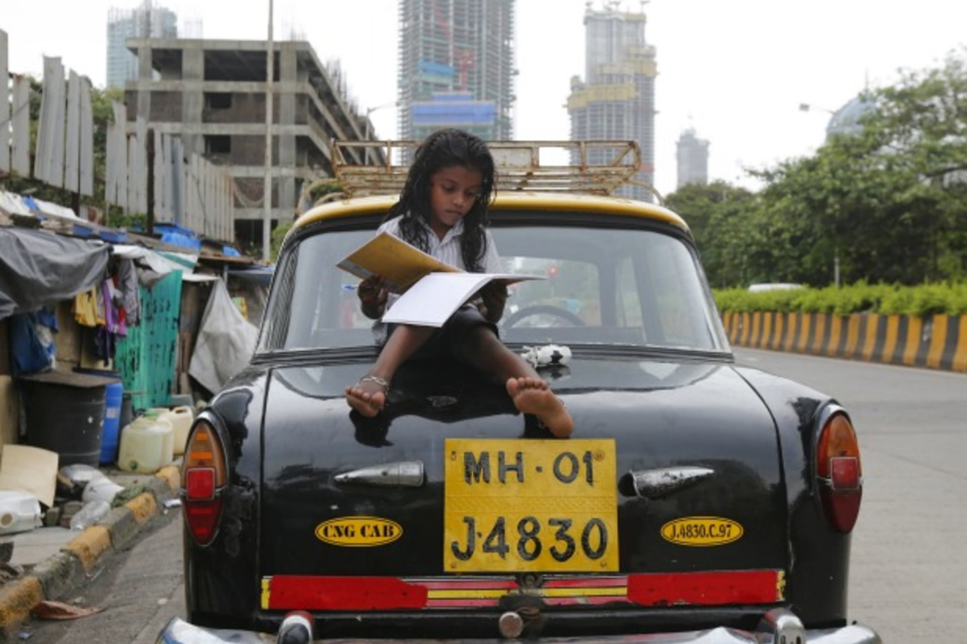 <p>A girl studies while sitting on top of a taxi outside her shanty home at a roadside in Mumbai, India (Shailesh Andrade/Reuters).</p>