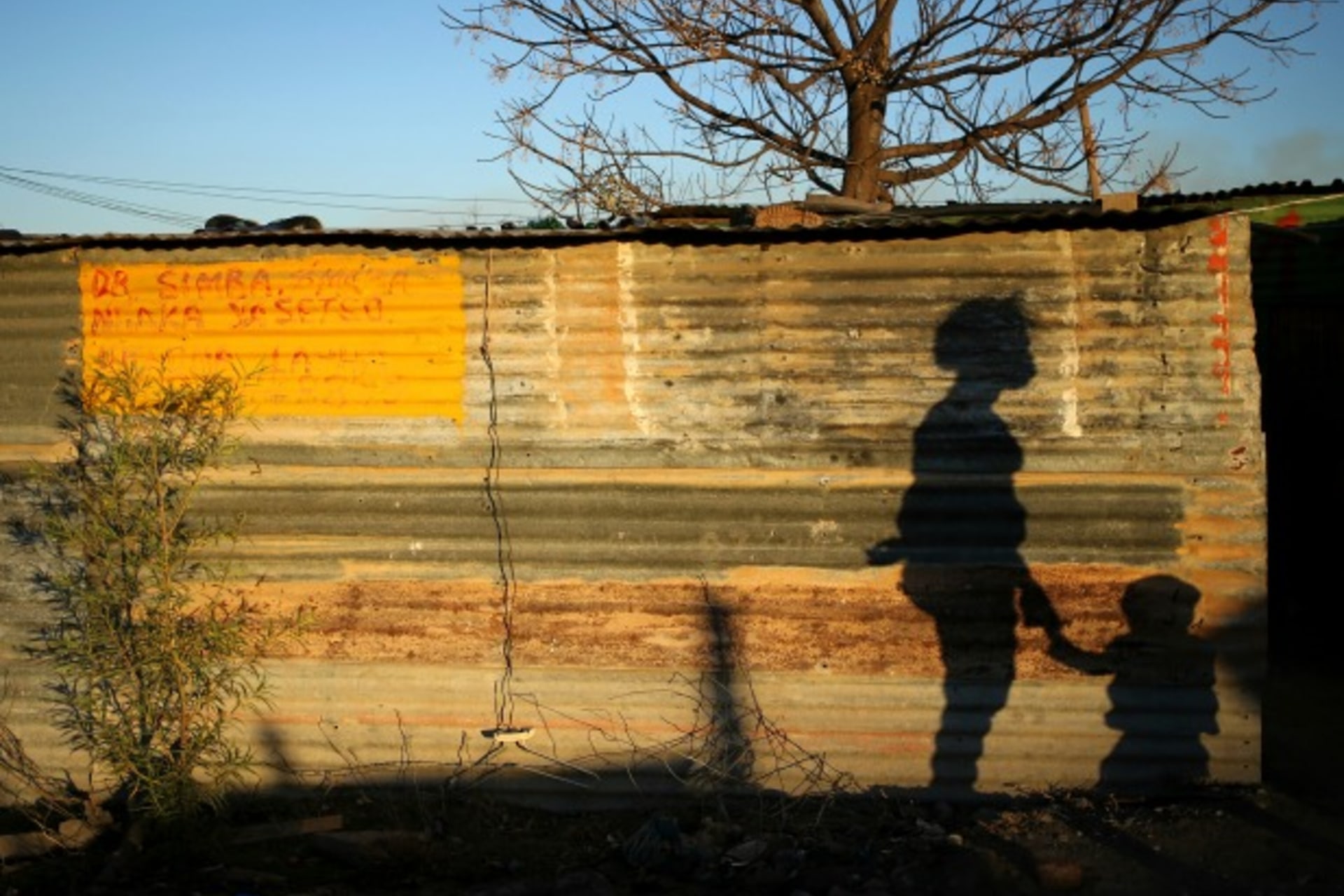 <p>The shadows of a mother and child are cast on a shack in Marikana’s Nkaneng township in Rustenburg,South Africa, August 2013 (Courtesy Reuters/Siphiwe Sibeko).</p>