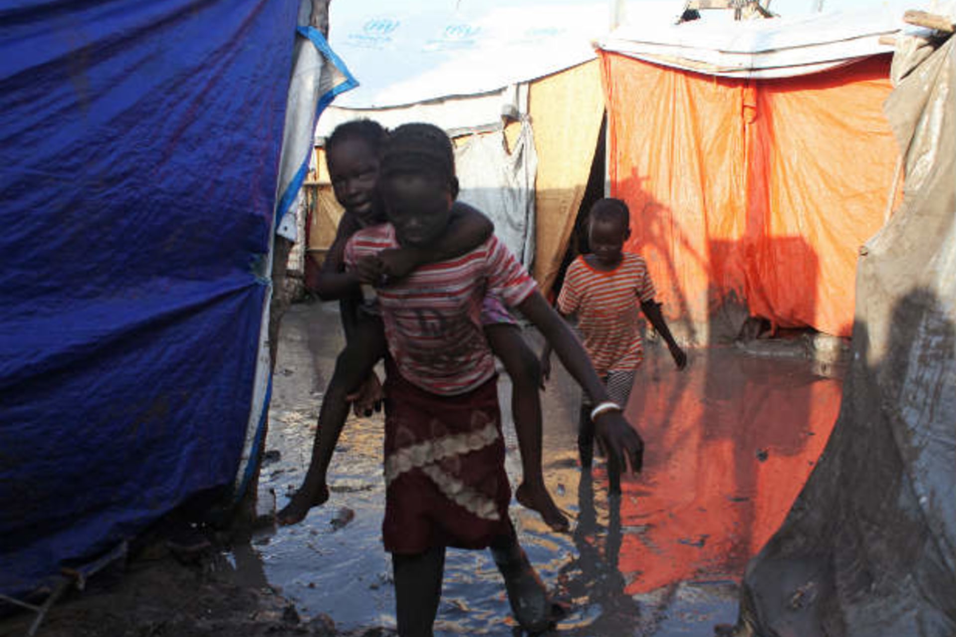 A South Sudanese girl displaced by the conflict carries a younger boy on her back as they walk through mud in a flooded camp for internally displaced people at the UNMISS base in Malakal, Upper Nile State, May 30, 2014.   (Andreea Campeanu/Cour