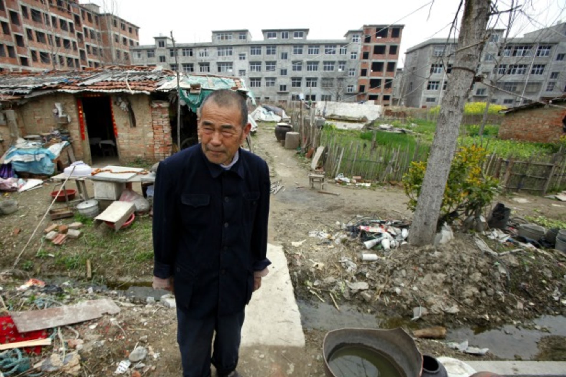<p>Farmer Xiang Wen Jiang stands in front of his house, surrounded by newly constructed residential buildings in the town of Gushi, Henan Province on March 28, 2010.</p>