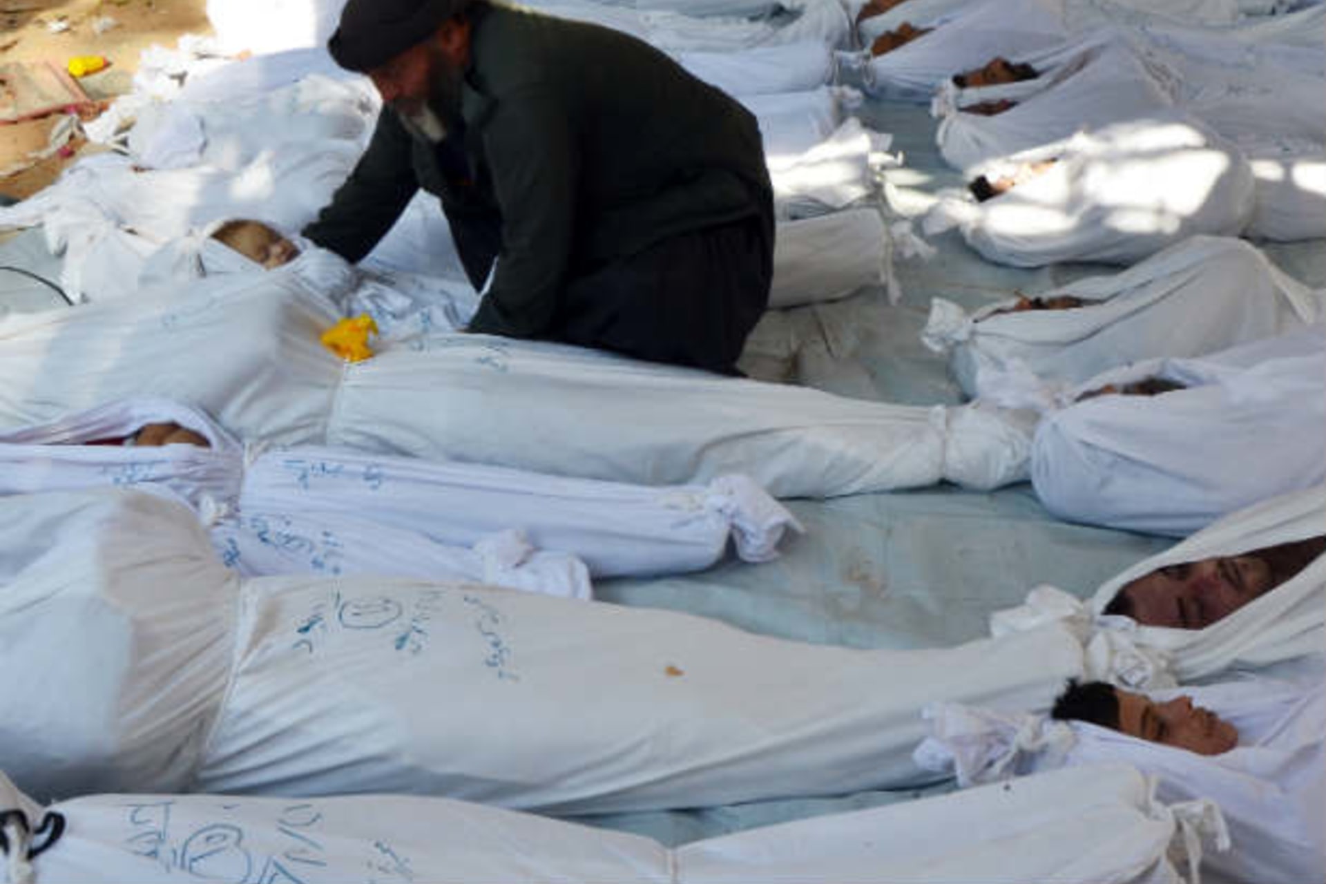 A man holds the body of a dead child among bodies of people activists say were killed by nerve gas in the Ghouta region, in the Duma neighbourhood of Damascus August 21, 2013 (Khabieh/Courtesy Reuters).