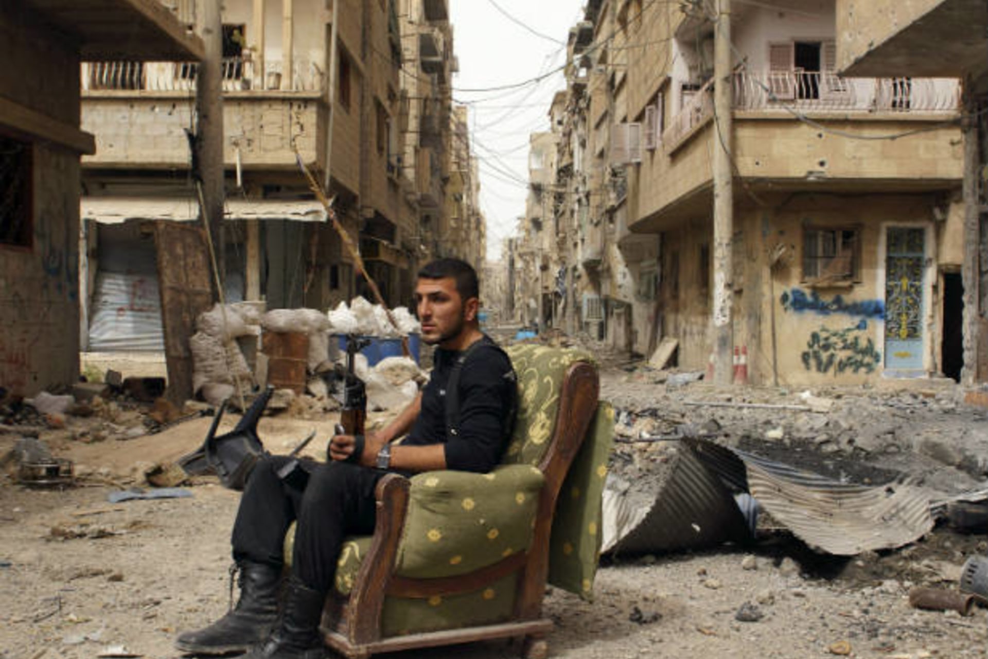 A member of the Free Syrian Army holds his weapon as he sits on a sofa in the middle of a street in Deir al-Zor April 2, 2013 (Ashawi/Courtesy Reuters).
