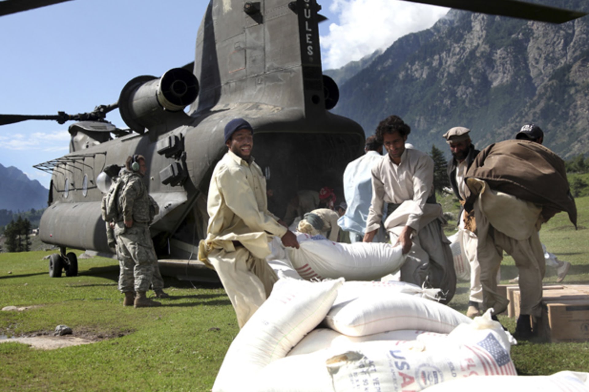 Pakistani men throw a bag of flour onto a pile out the back of a U.S. Army Chinook helicopter in Khyber Pakhtunkhwa province