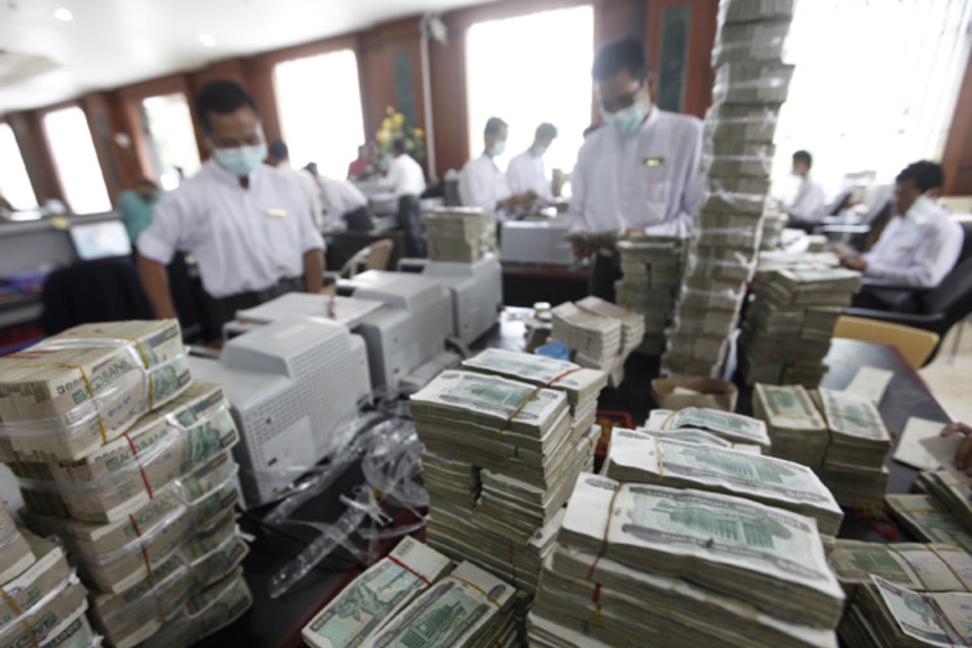 <p>Cashiers are seen behind piles of kyat banknotes as they count it in a private bank in Yangon.</p>
