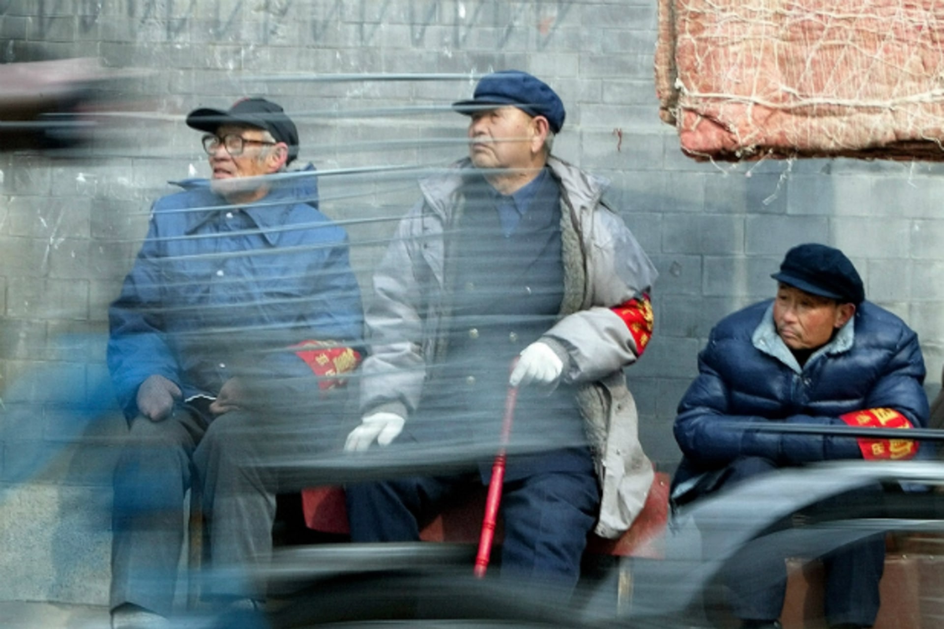 <p>Chinese cyclists ride past three elderly men from neighborhood watch committees in central Beijing on February 27, 2003.</p>
