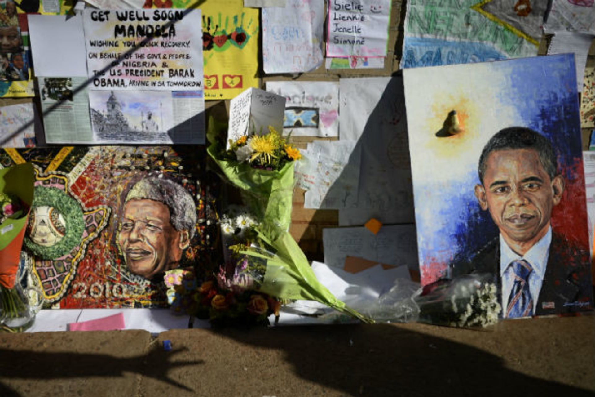 Wellwishers cast shadows in front of portraits of Nelson Mandela (L) and U.S. President Barack Obama outside the Medi-Clinic Heart Hospital, where the ailing former South African President is being treated, in Pretoria June 28, 2013.