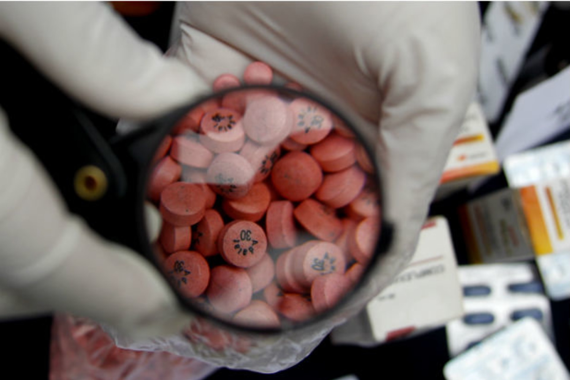 <p>A Peruvian official examines seized counterfeit pills through a magnifying glass in Lima in August 2010.</p>
