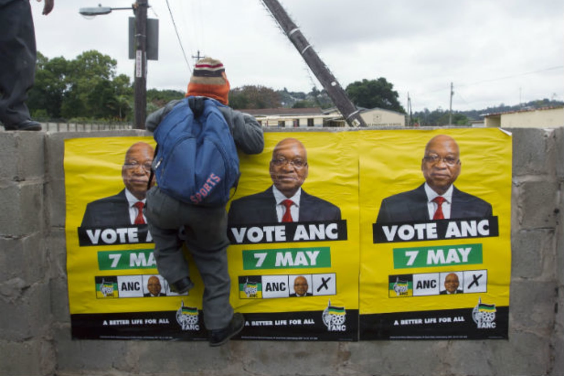 African National Congress (ANC) election posters featuring images of South Africa's President Jacob Zuma are displayed on a wall as a school boy climbs over it in Embo May 6, 2014.