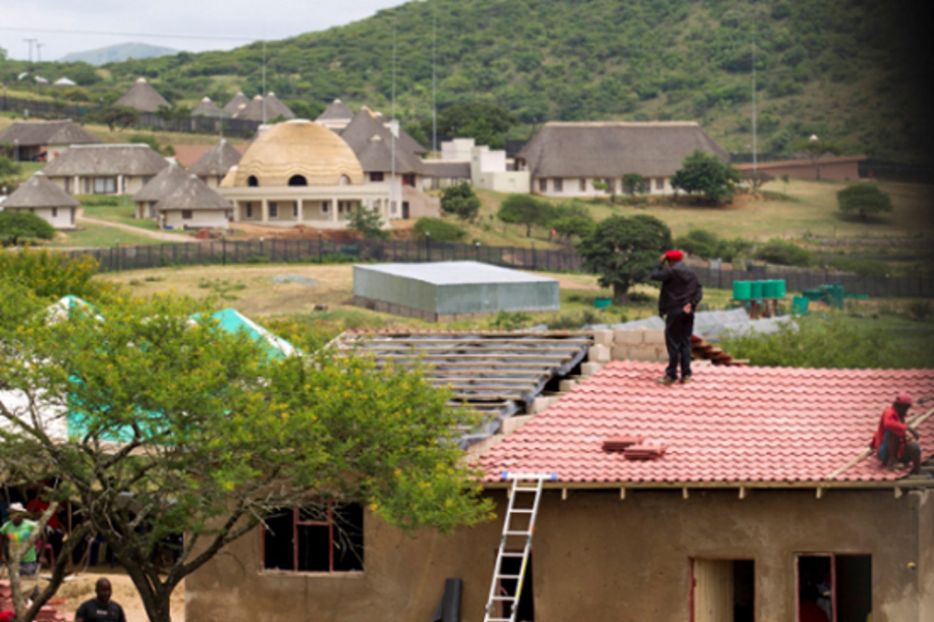 A member of the Economic Freedom Fighters (EFF) stands on the roof of a house they built for an elderly woman, near the homestead of South African President Jacob Zuma (in the background), in Nkandla January 11, 2014.