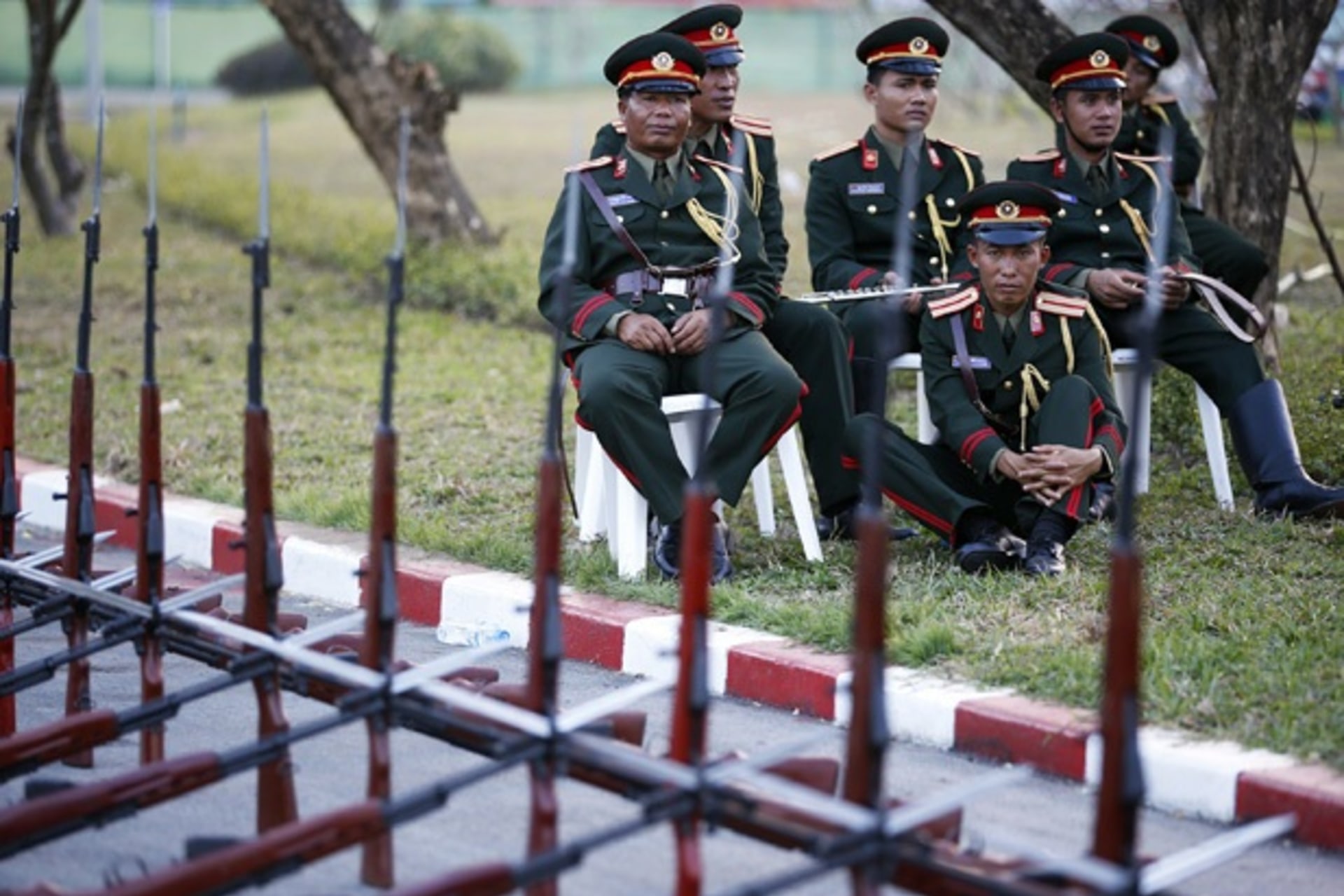 Laos honor guards and members of military orchestra sit behind guns as they prepare to welcome another foreign delegation arriving at Vientiane airport.