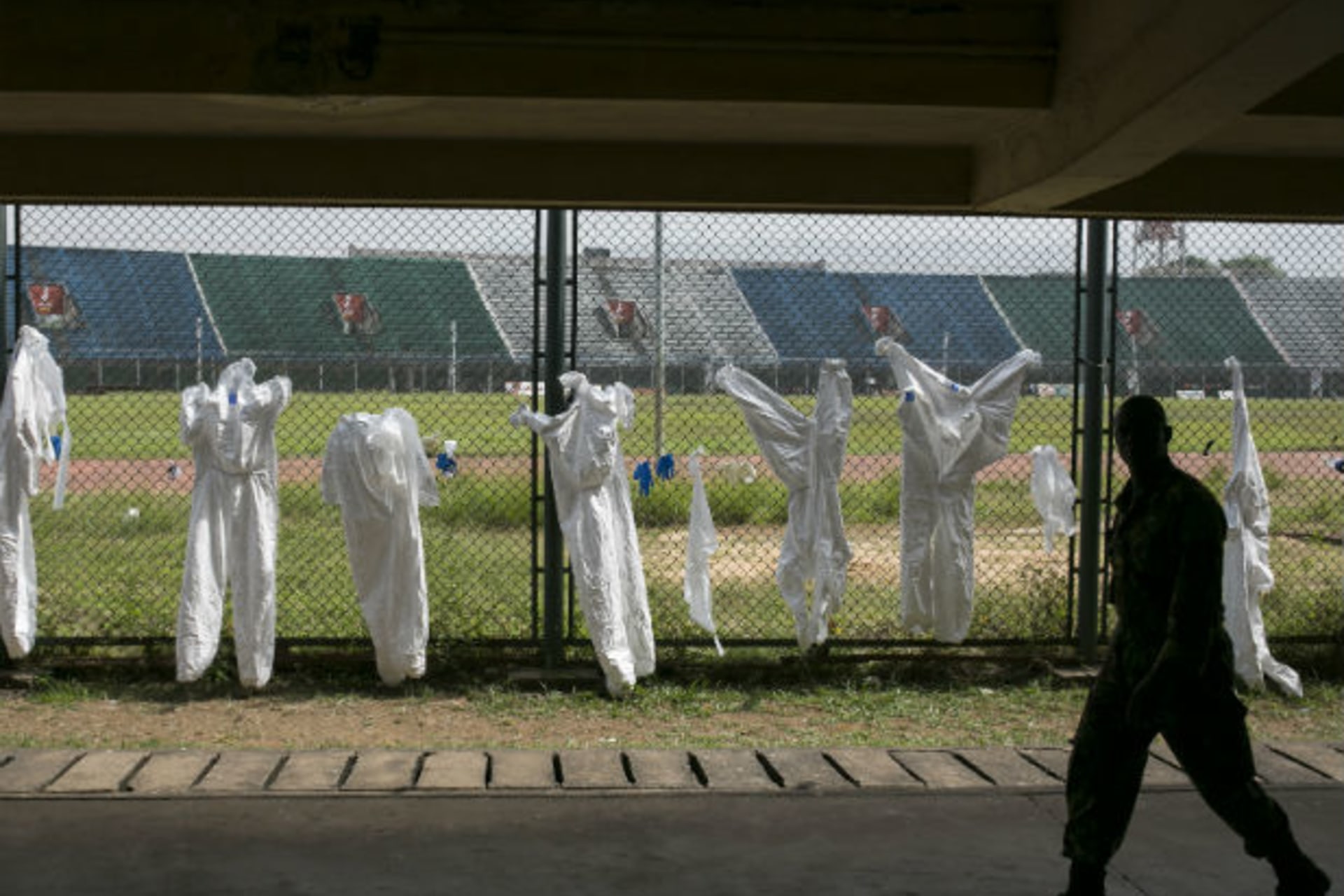 <p>A Sierra Leonean soldier walks past protective clothing drying on a fence in the Ebola Training Academy in Freetown, Sierra Leone, on December 16, 2014.</p>