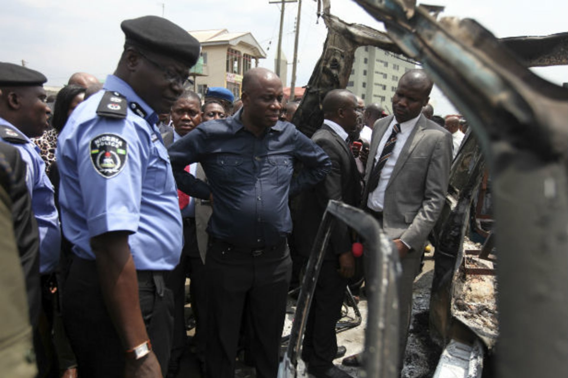Nigerian River state governor Amechi stands with security officials to assess a burnt commercial bus (Akintunde Akinleye/Courtesy Reuters).