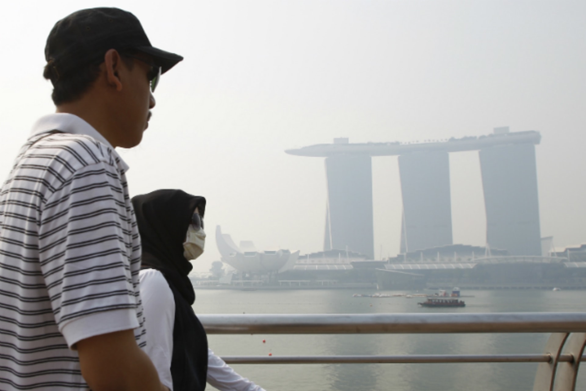 <p>A tourist wearing a face mask passes the hazy skyline of the Marina Bay Sands casino and resort in Singapore on June 18, 2013. (Edgar Su/Courtesy Reuters)</p>
