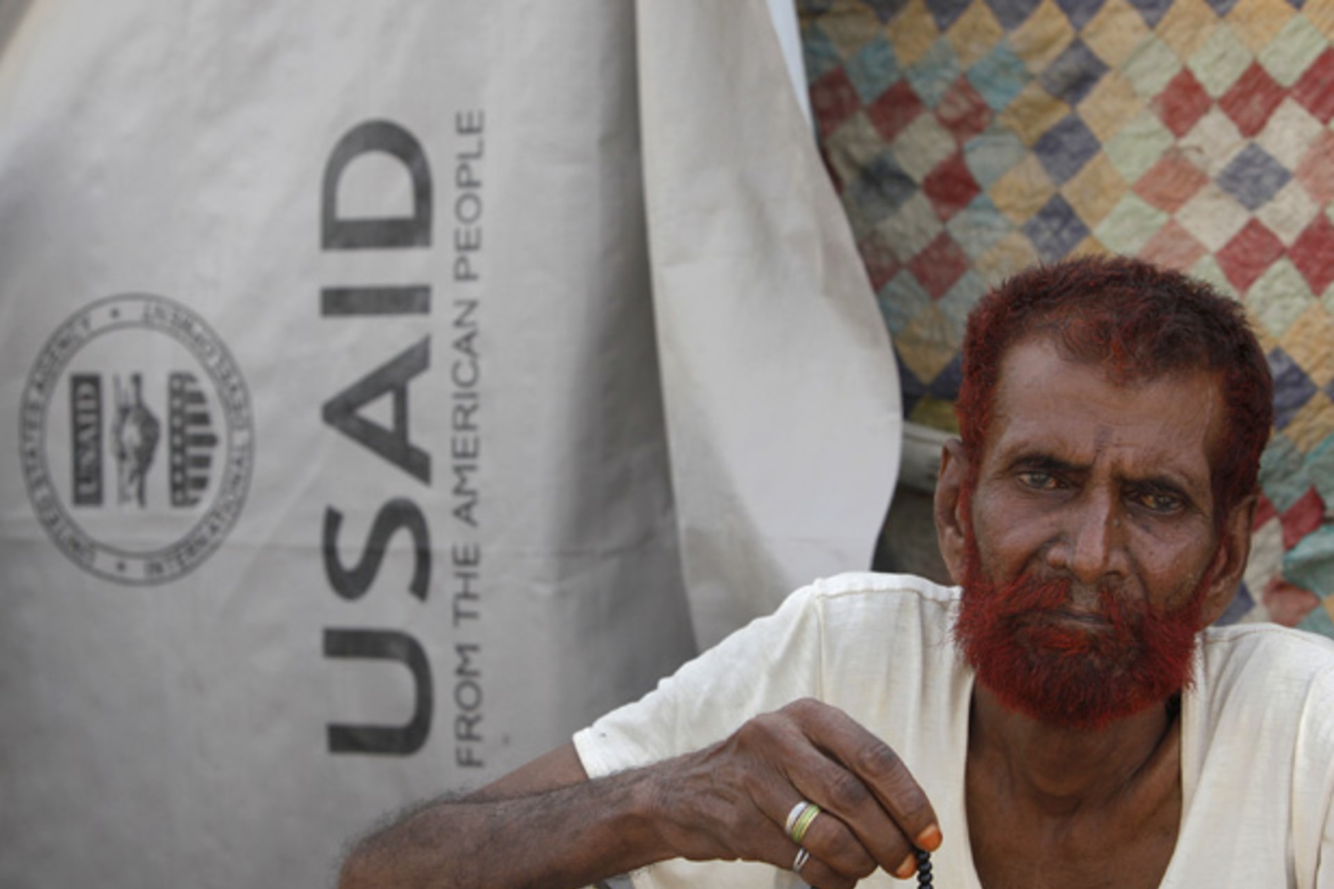 Flood victim Haji Usman holds praying beads as he sits outside his makeshift tent covered by weather sheet donated by USAID while taking refuge on an embankment at Chandan Mori village in Dadu