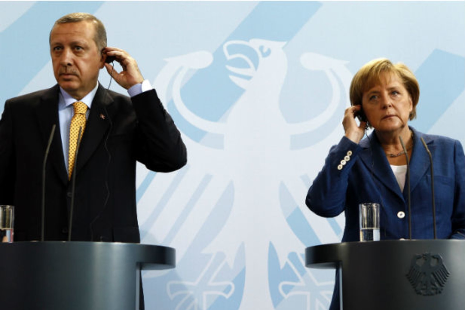 Turkey's PM Erdogan and German Chancellor Merkel adjust their earphones for the translations as they address a news conference following their bilateral talks in Berlin (Fabrizio Bensch/Courtesy Reuters)