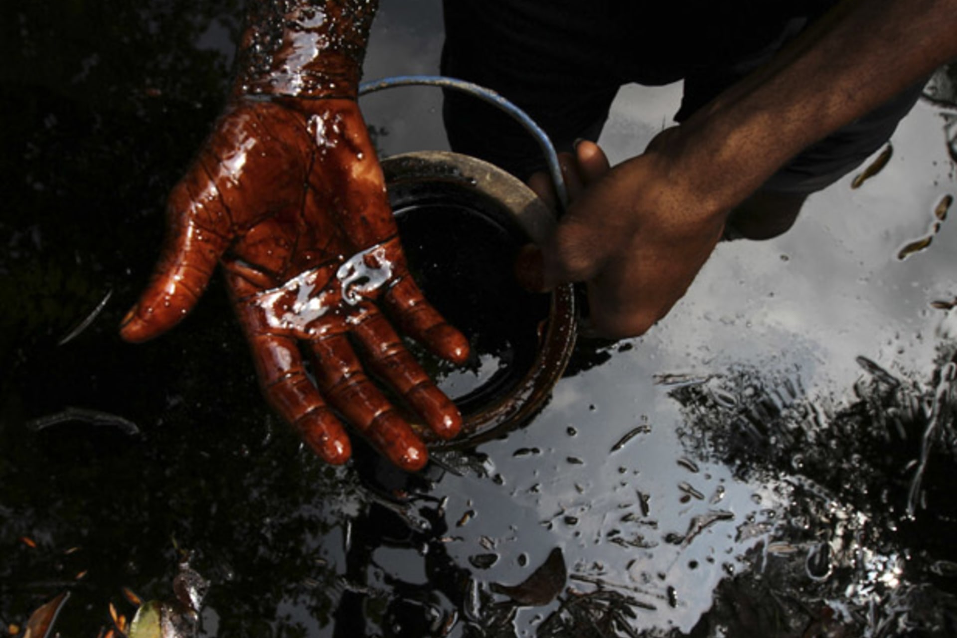 A man samples crude oil at the bank of a polluted river in Bidere community in Ogoniland in Nigeria's delta region