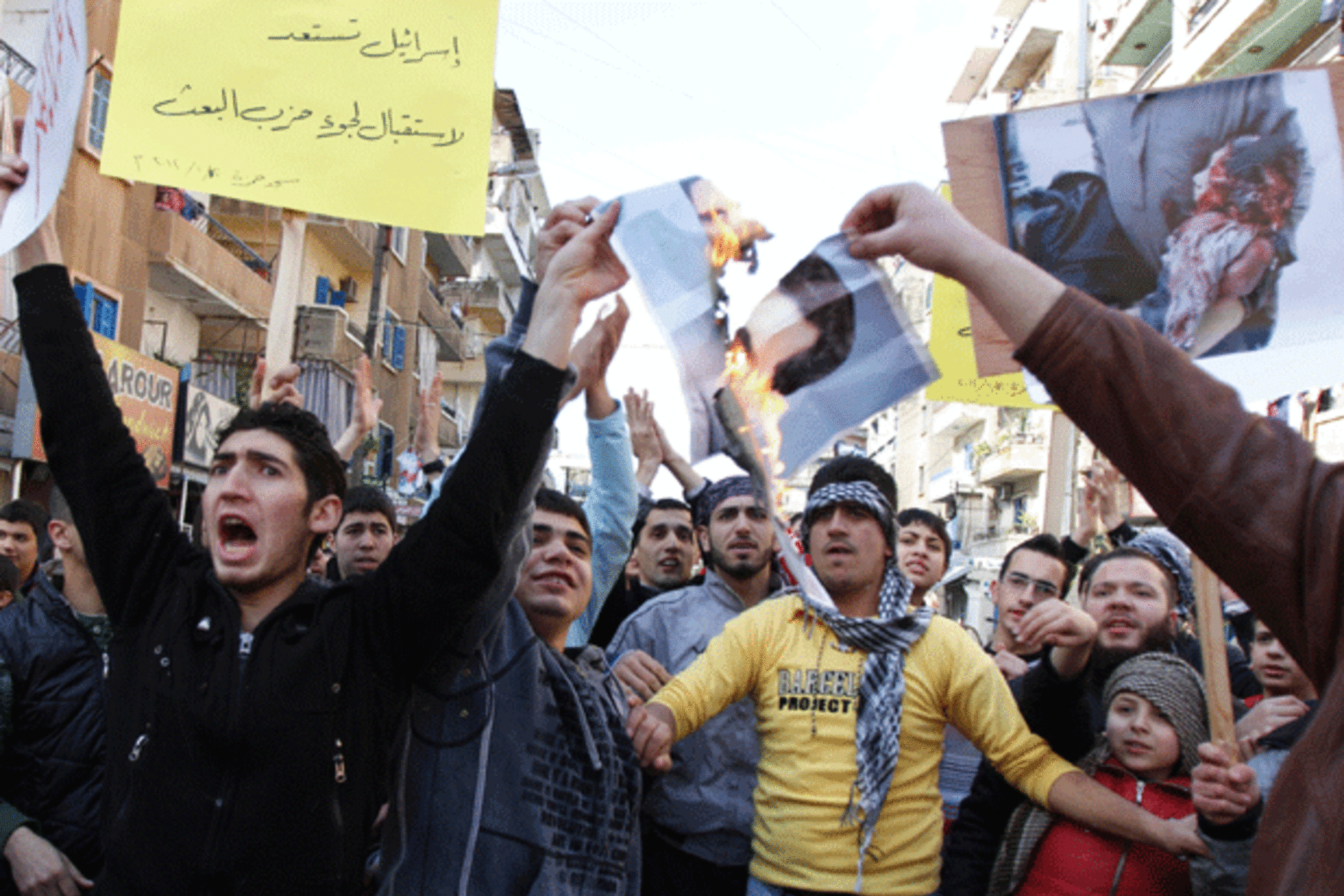<p>Lebanese and Syrian protesters in northern Lebanon carry banners and burn a picture of Syrian President Bashar al-Assad as they march in solidarity with Syria’s anti-government protesters on January 20, 2012. (Omar Ibrahim/courtesy Reuters)</p>
