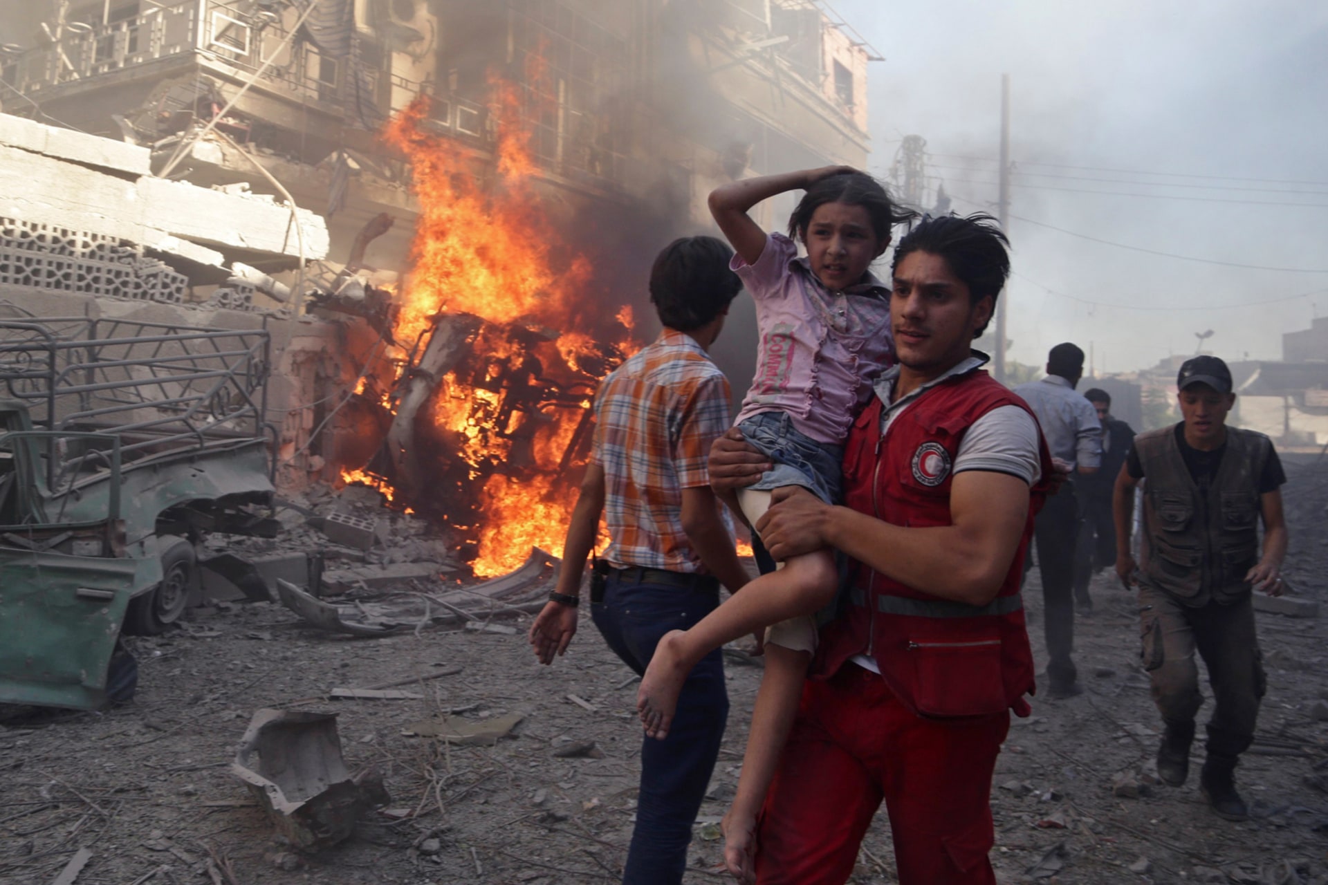 <p>A member of the Syrian Arab Red Crescent carries a girl as they rush away from a site hit by what activists said were airstrikes by forces loyal to Syria’s President Bashar al-Assad in the Douma neighborhood of Damascus, Syria, on August 24, 2015.</p>
