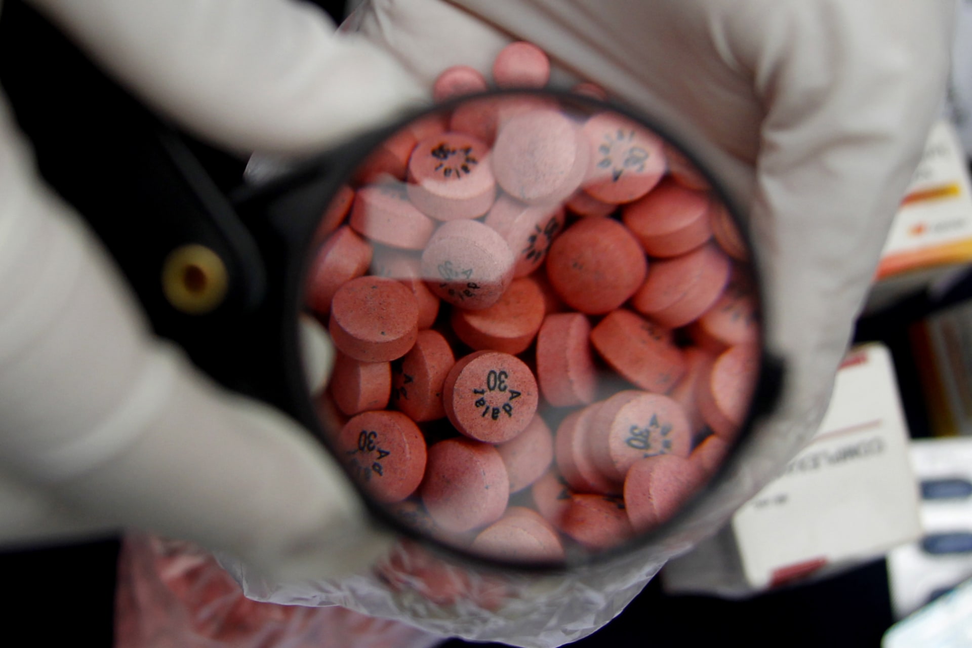 <p>A Peruvian Health Ministry worker shows the media seized counterfeit pills through a magnifying glass in Lima on August 5, 2010.</p>
