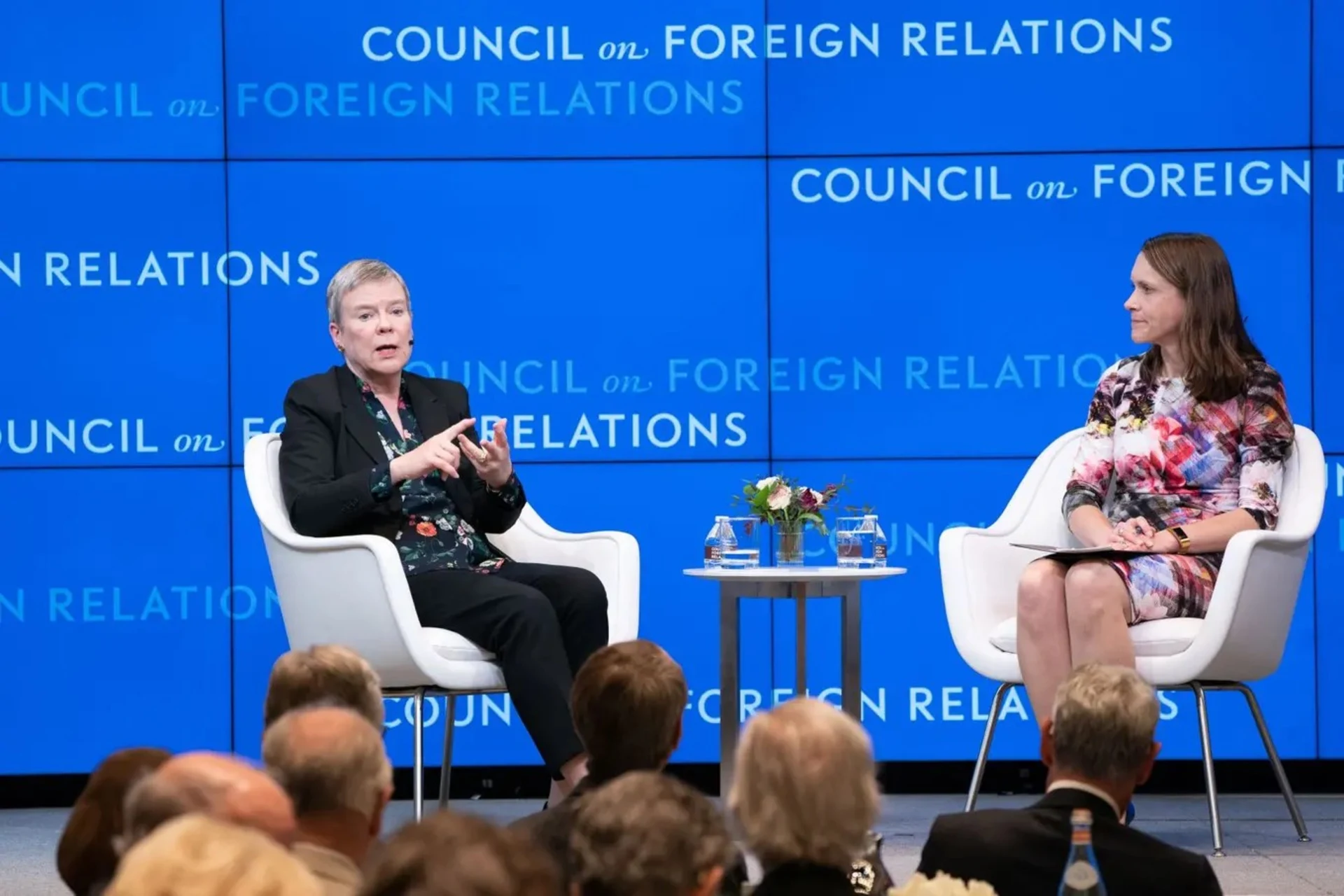 Two people sitting on a stage with a blue background.