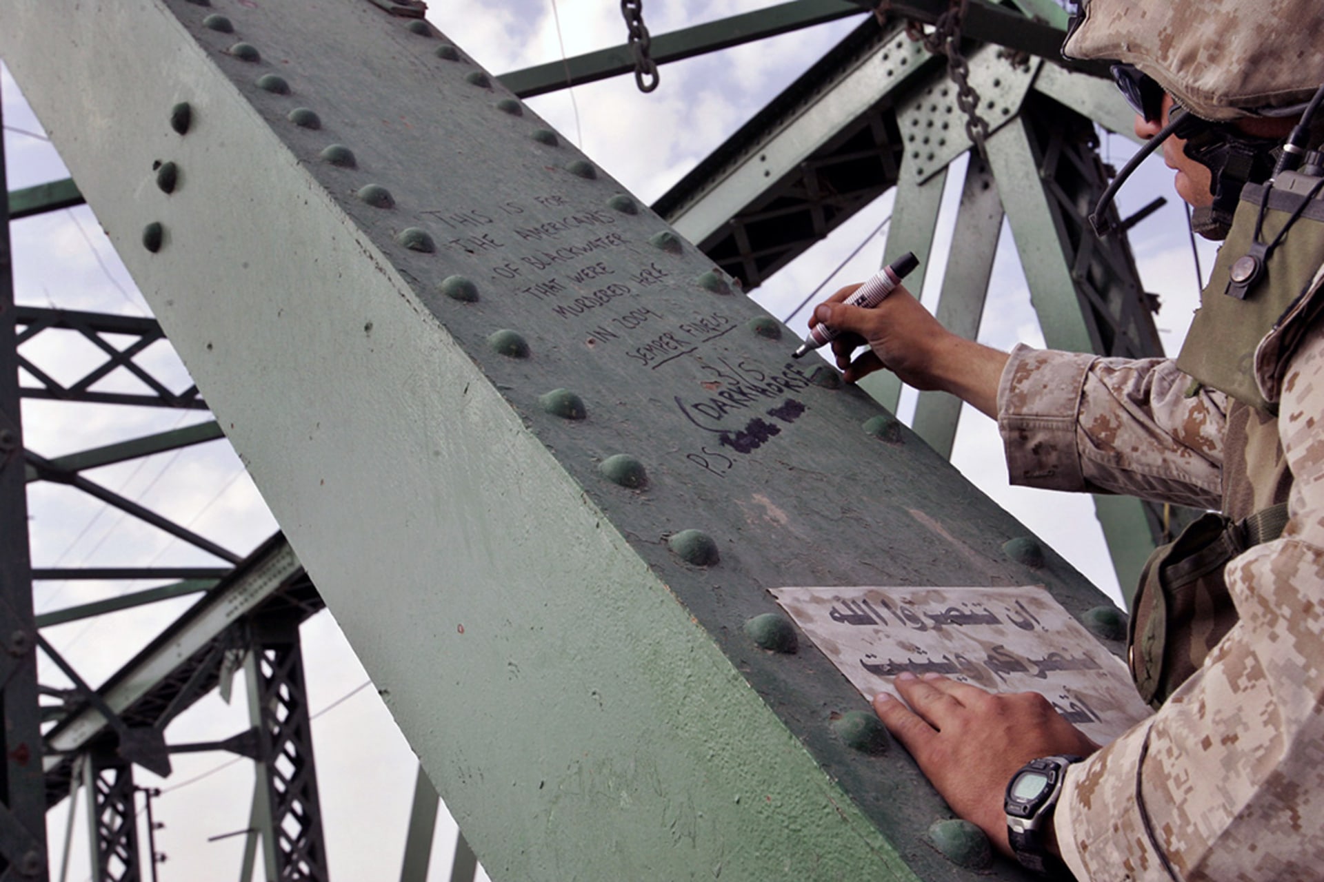 A U.S. marine writes a tribute on a bridge in Fallujah, Iraq, where the bodies of murdered American contractors were hung. 
