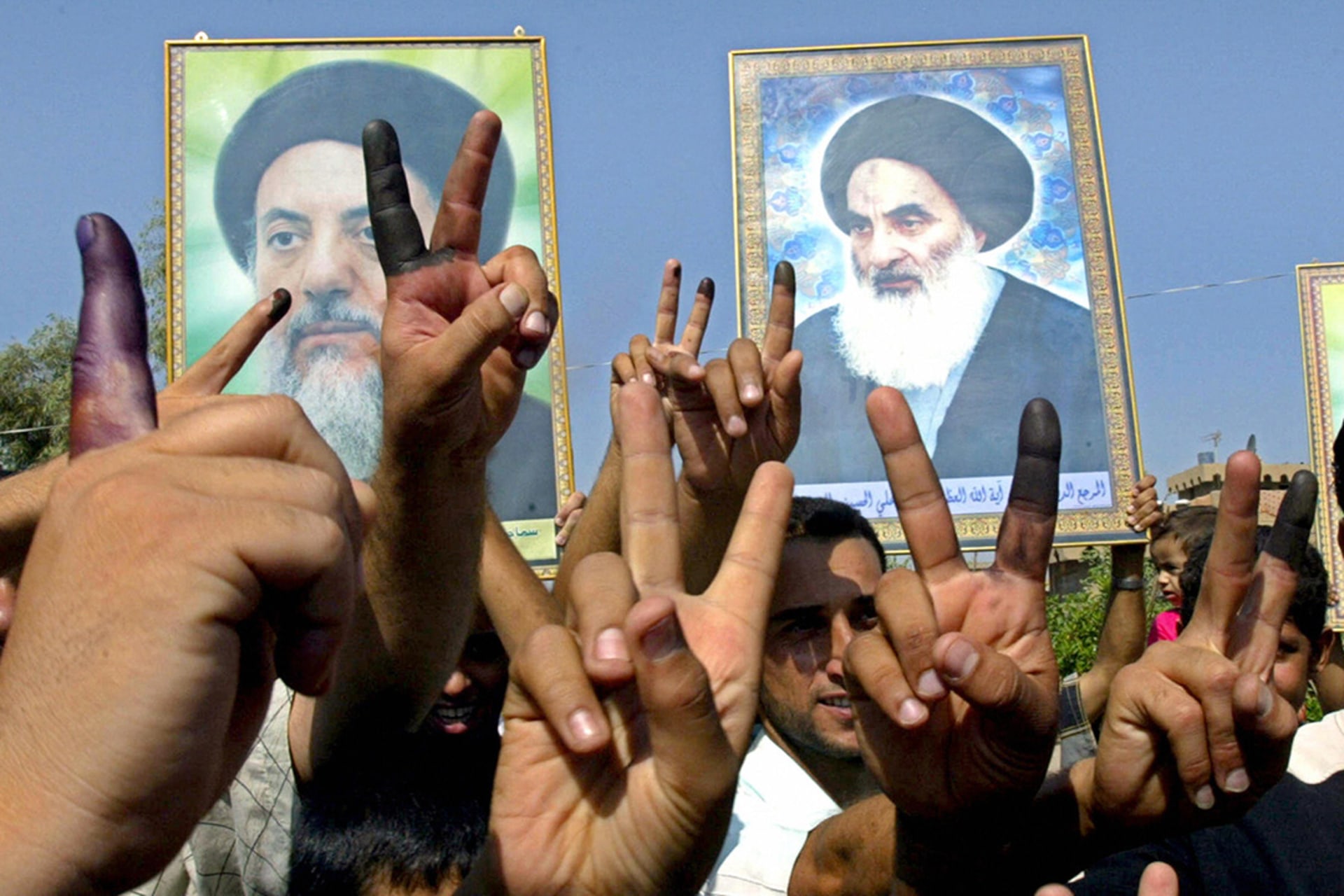 Iraqis show their ink-stained fingers and raise pictures of Grand Ayatollah Ali al-Sistani and the late Mohammed Baqir al-Hakim after voting in Baghdad. 
