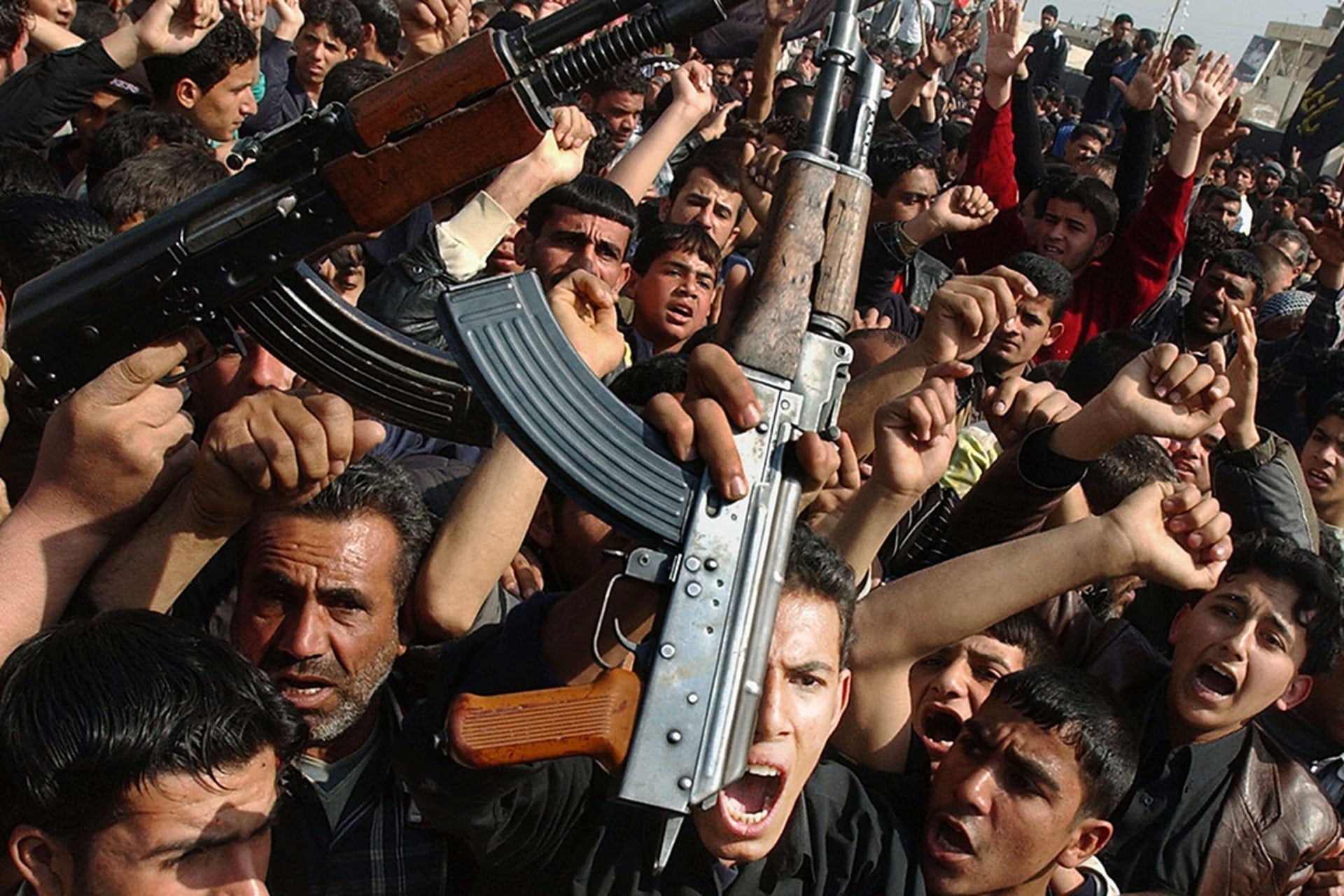 Shiite Muslims brandish weapons as they protest the bombing of a Shiite holy shrine in Baghdad.