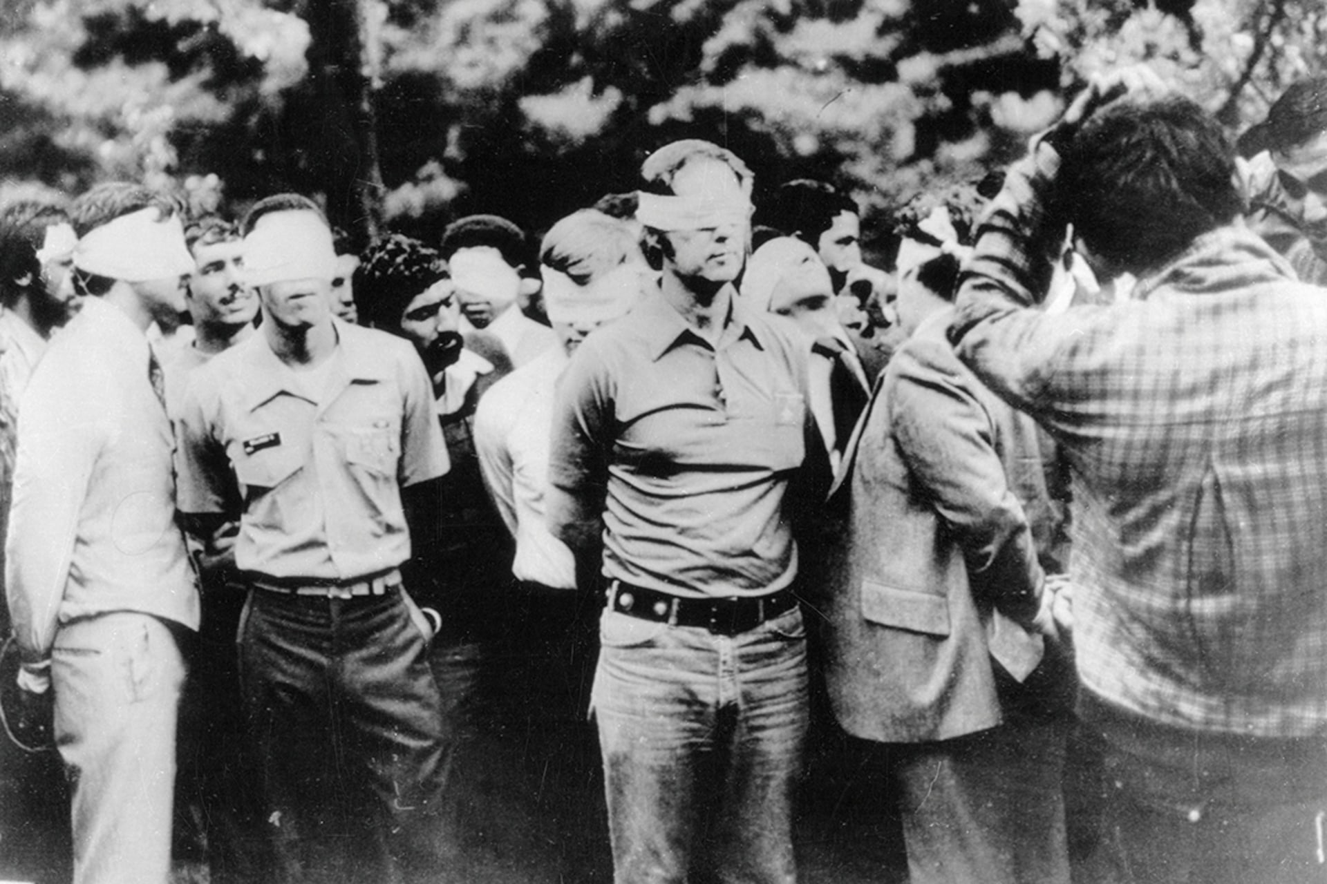Blindfolded American hostages and their Iranian captors stand outside the U.S. embassy in Tehran.