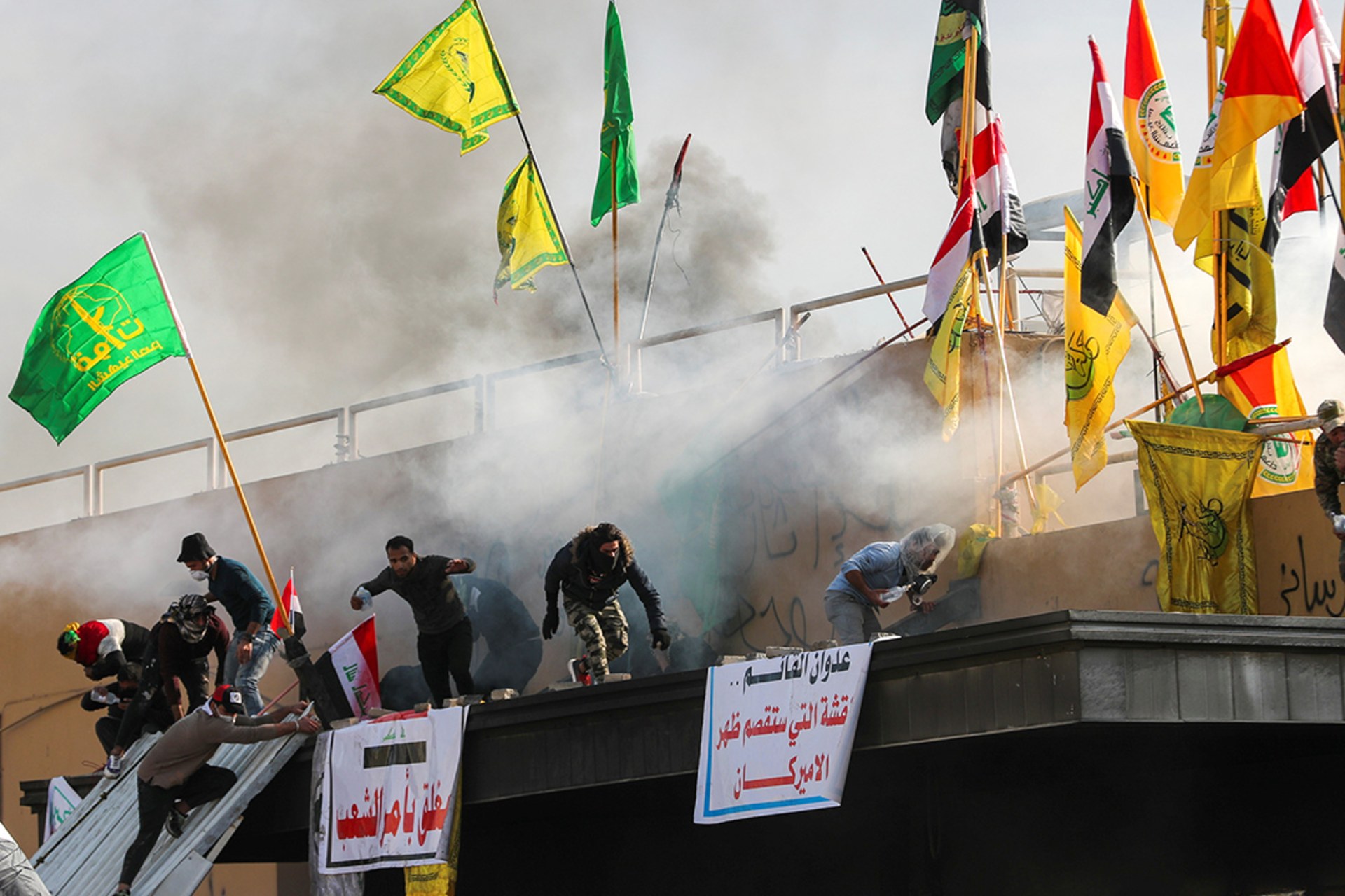 Protesters and militia fighters run from tear gas thrown by U.S. embassy security forces during a protest condemning U.S. air strikes.
