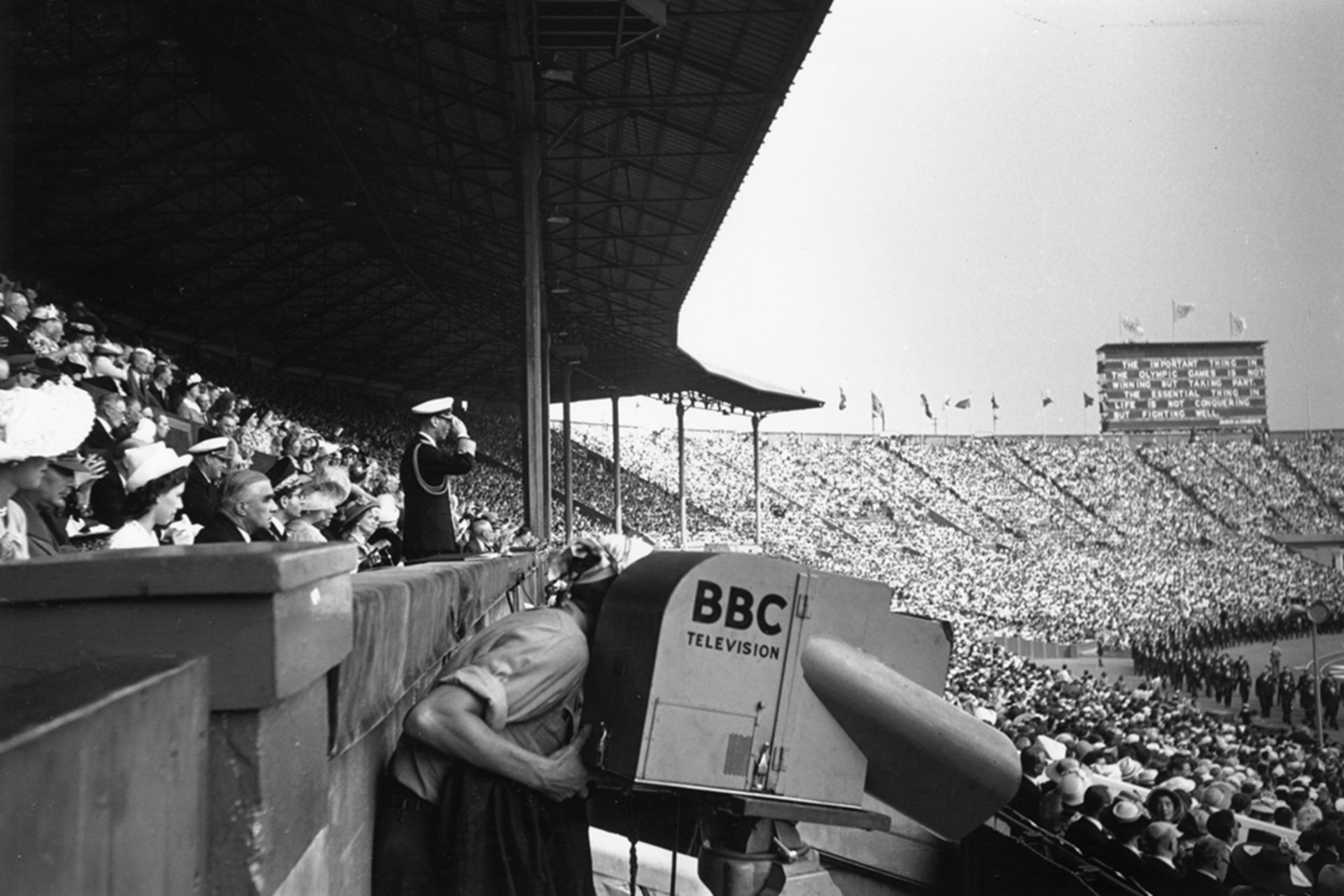 A BBC camera operator films the 1948 opening ceremony in London as British King George VI salutes in the background.