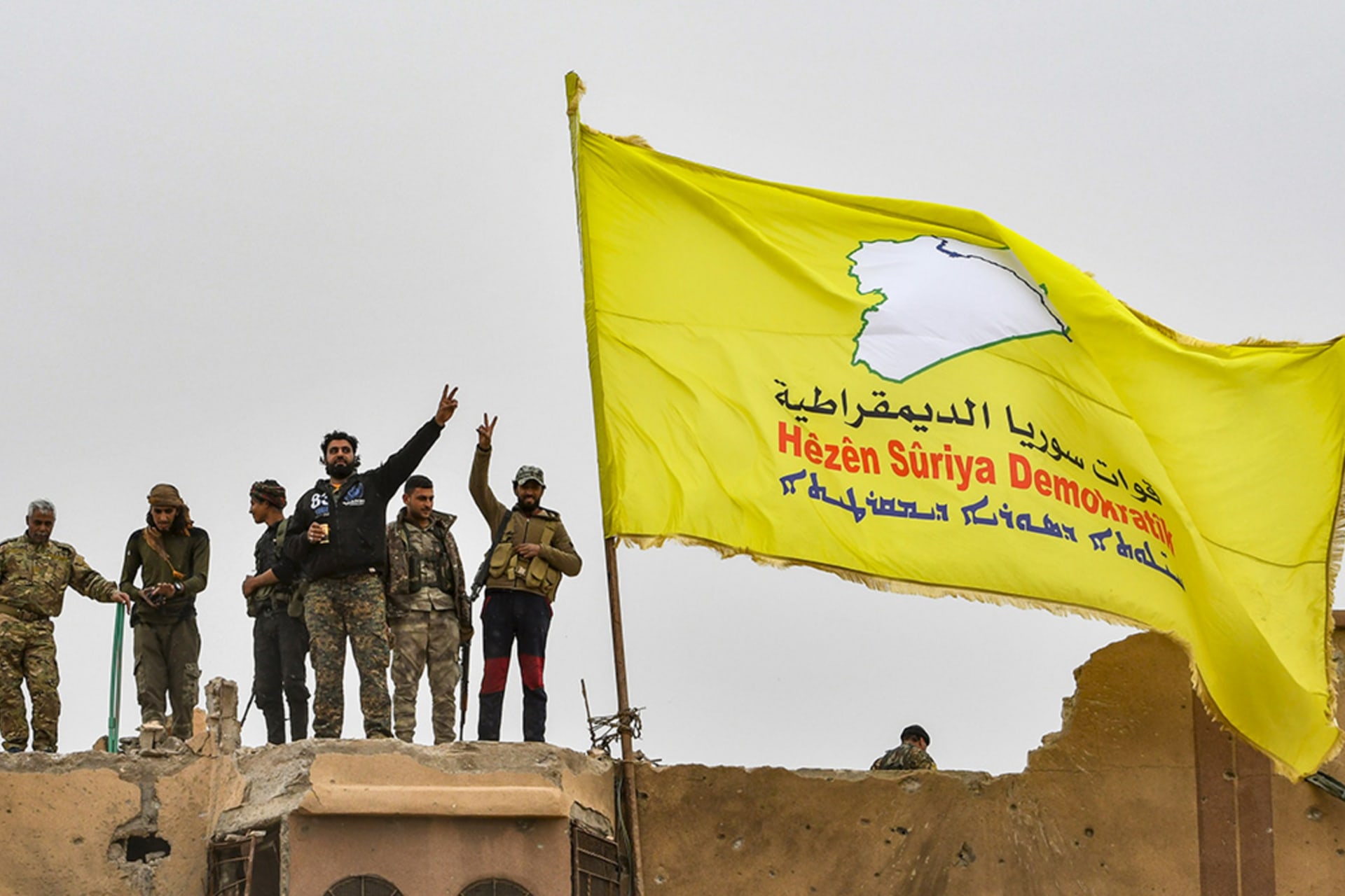 Fighters from the Syrian Democratic Forces (SDF) fly a flag in Baghouz, Syria. 
