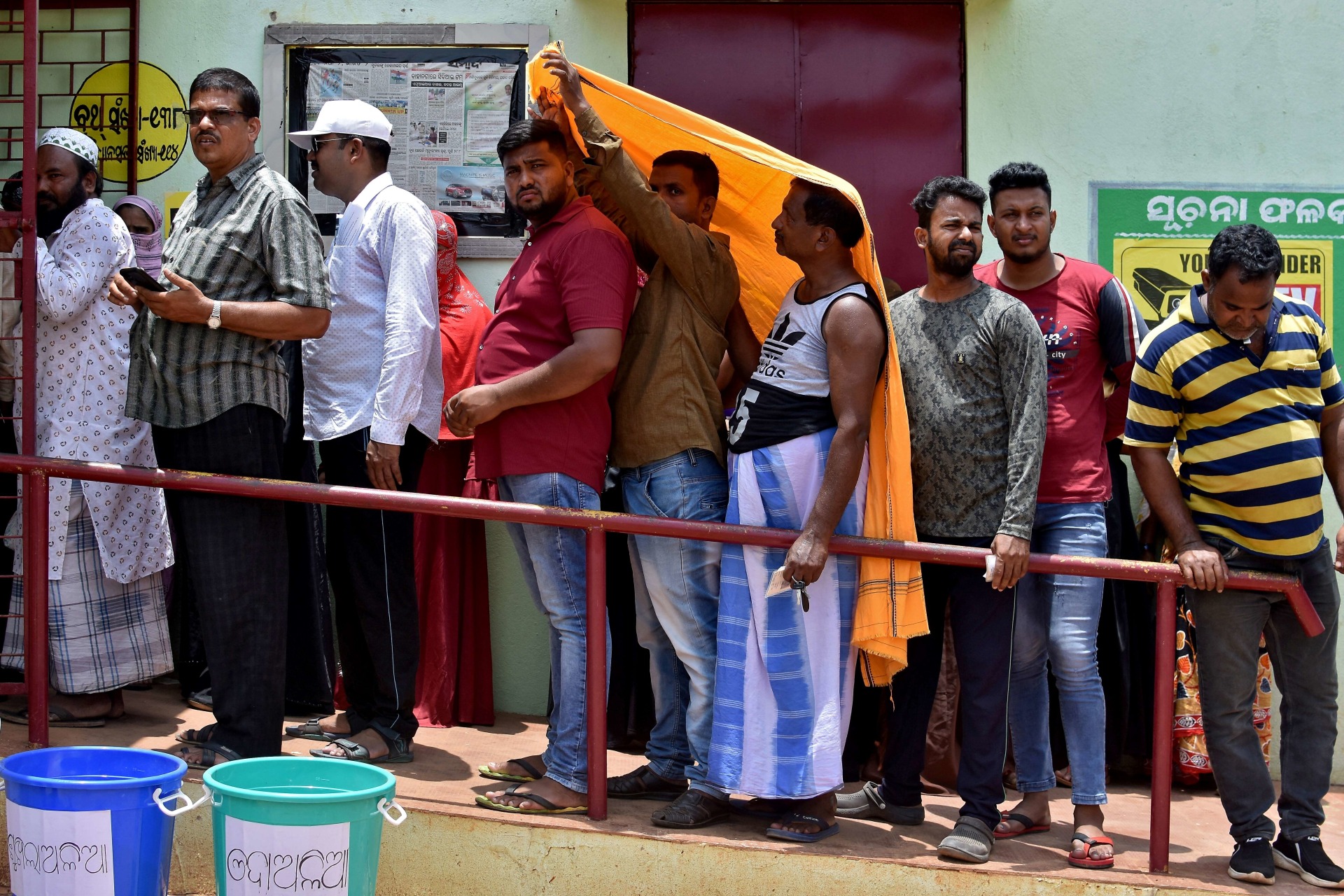 <p>Men use a stole to cover from heat as they wait in a line outside a polling station to cast their votes in Bhubaneswar, India.</p>
