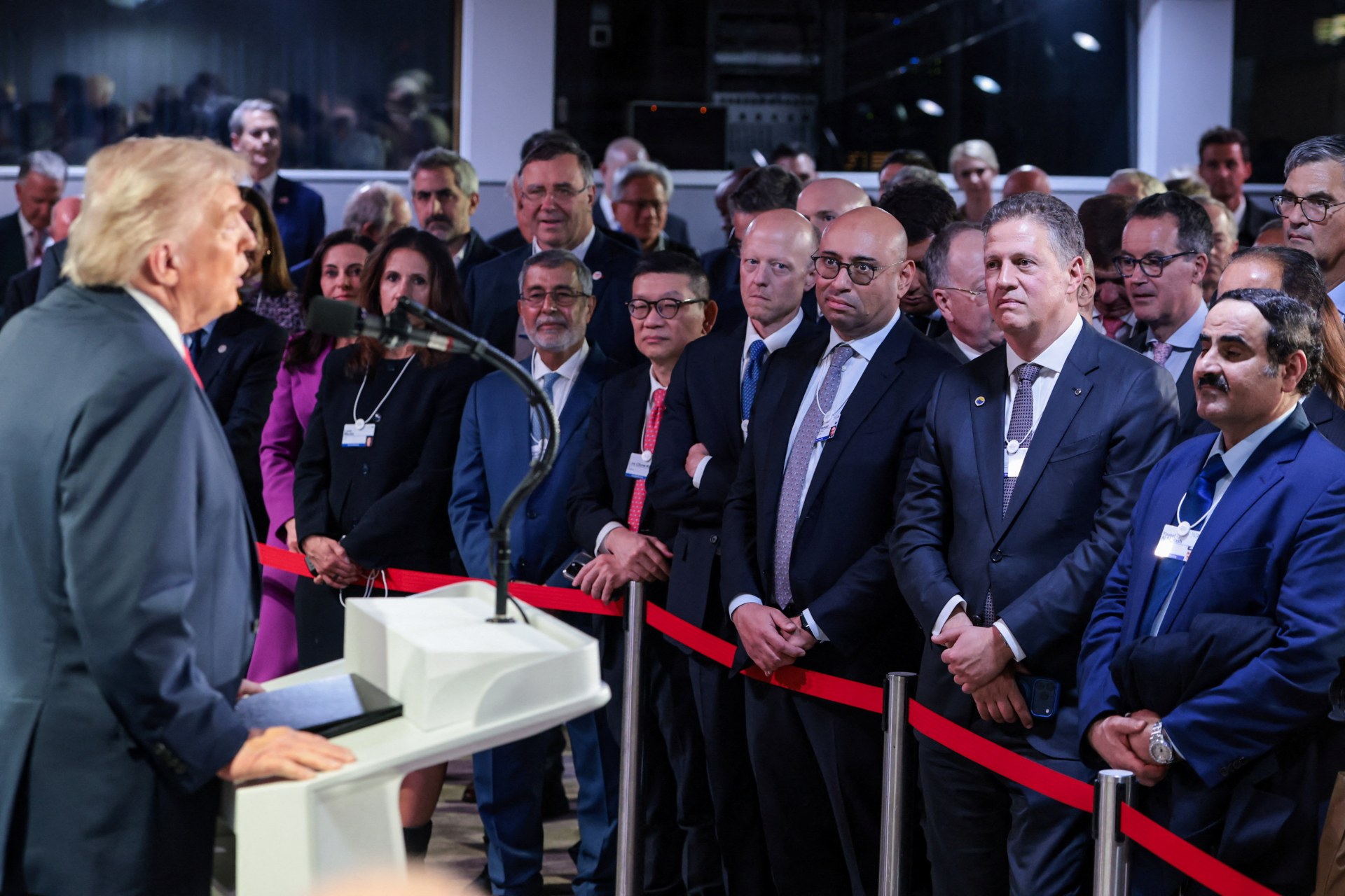 A crowd of Davos attendees in suits listen to President Donald Trump speaking at a podium