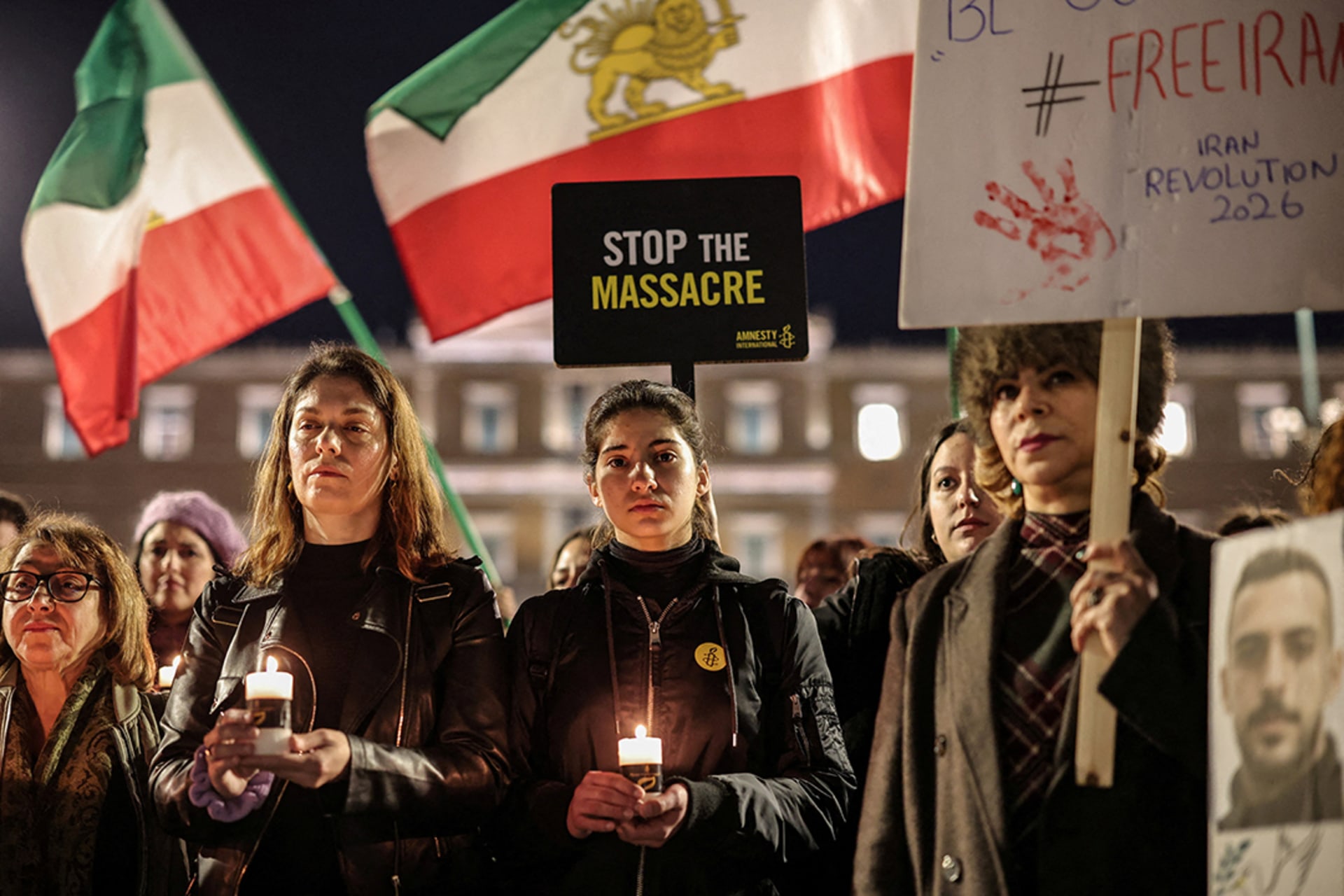 Activists stand in a line holding Iranian flags, candles, and signage to peacefully protest the Iranian crackdowns on civilian demonstrations in front of the Greek Parliamentary building.